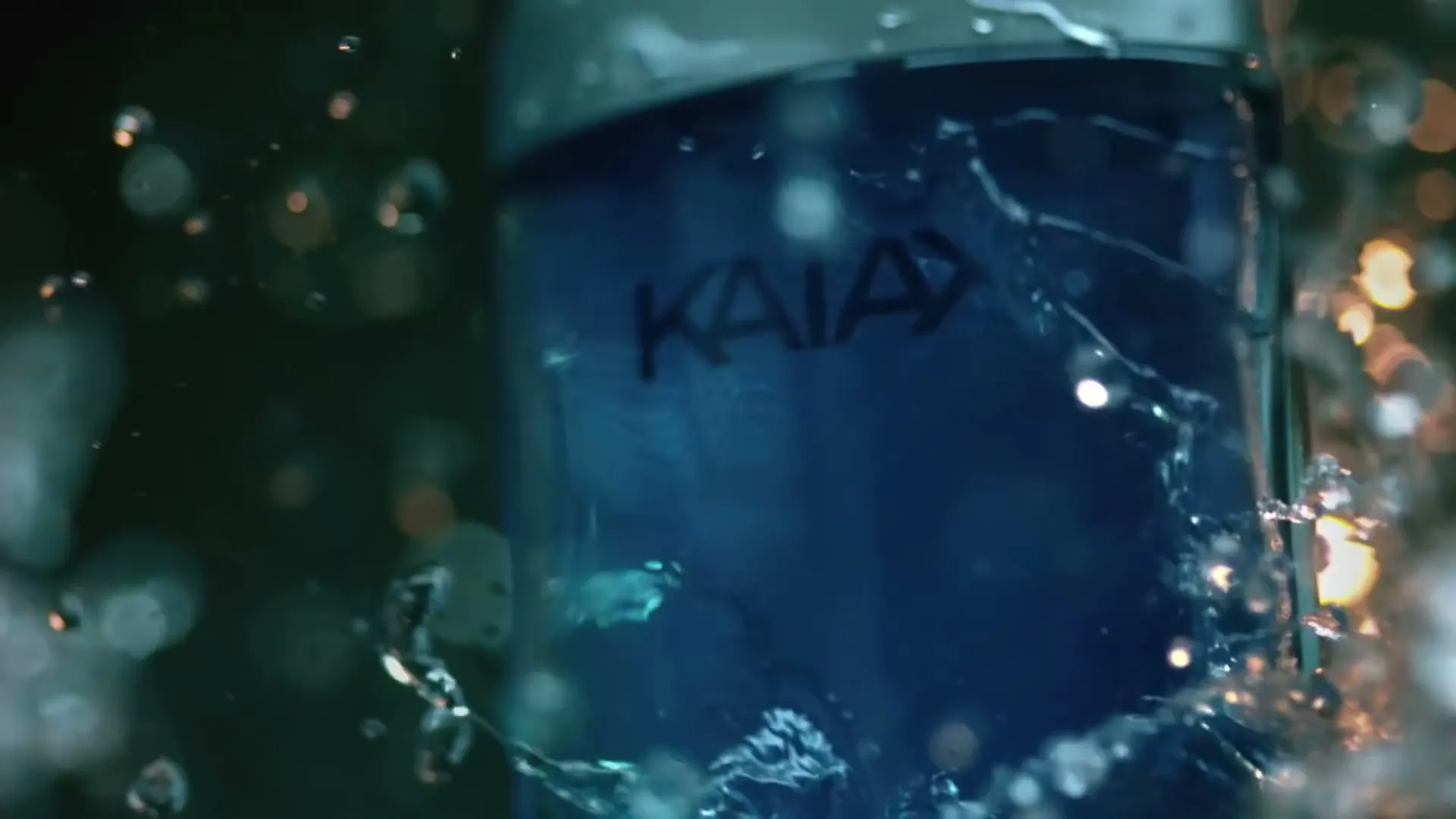 A blue perfume bottle with the word "KAIAK" on it is surrounded by splashing water, creating a dynamic and refreshing visual.