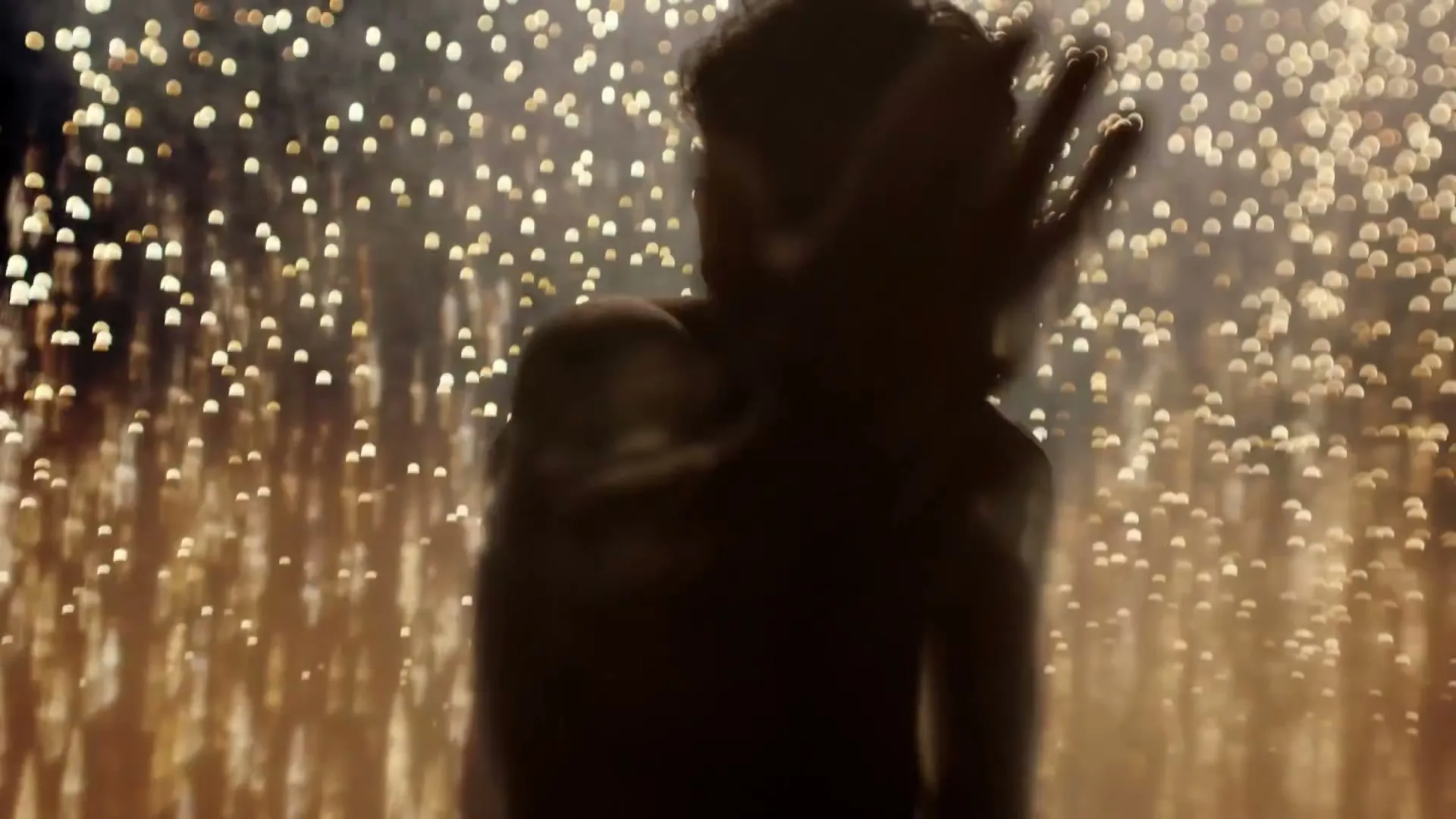 A person is silhouetted against a background of sparkling lights, raising their hand as if dancing or celebrating.
