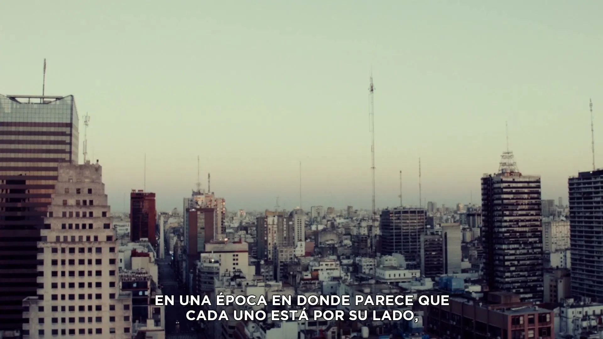 An aerial view of a city skyline with numerous buildings and antennas, under a pale sky, with text overlayed.