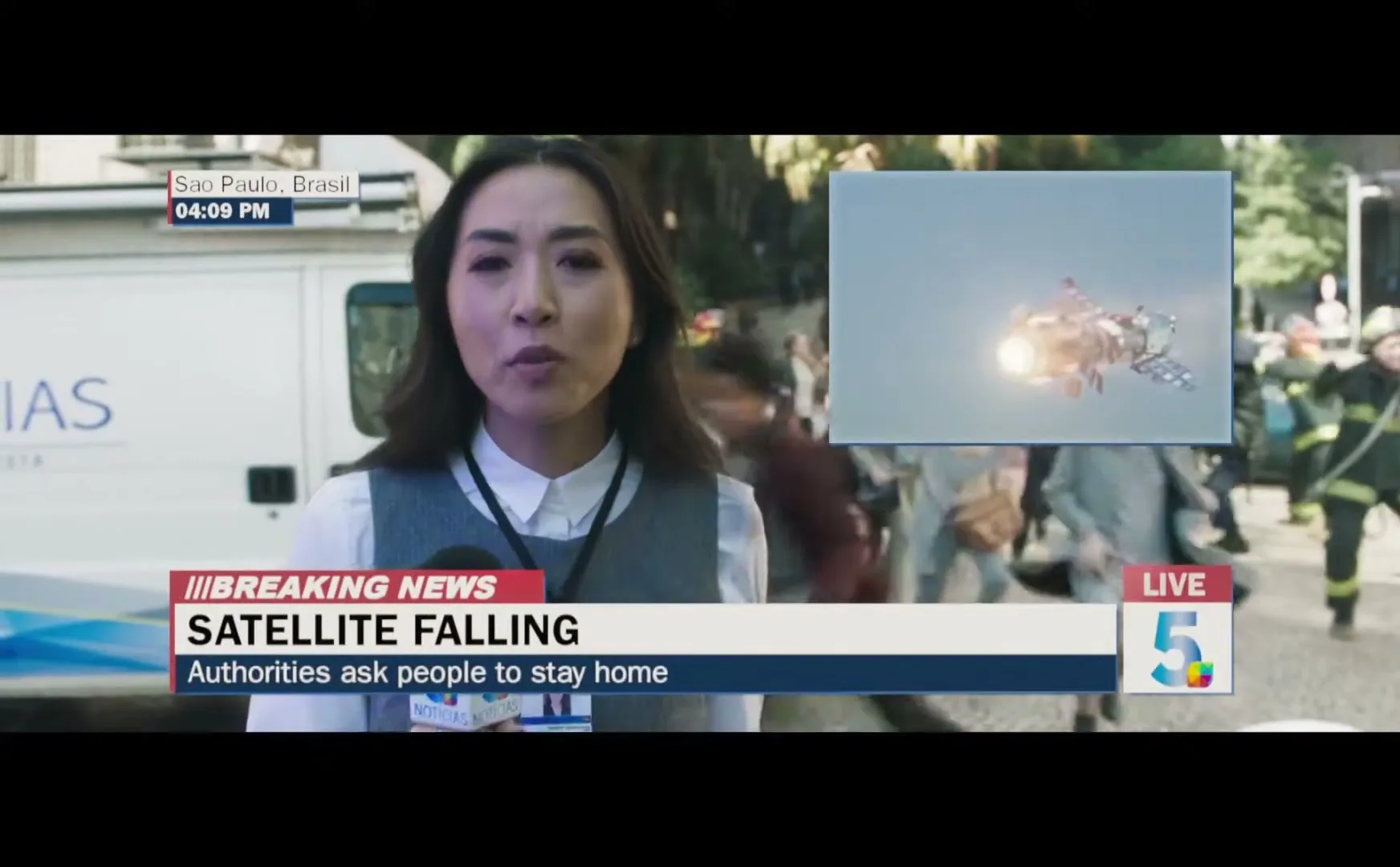 A female reporter in a white shirt and grey vest reports live from a chaotic street in Sao Paulo, Brazil, as a satellite falls from the sky.