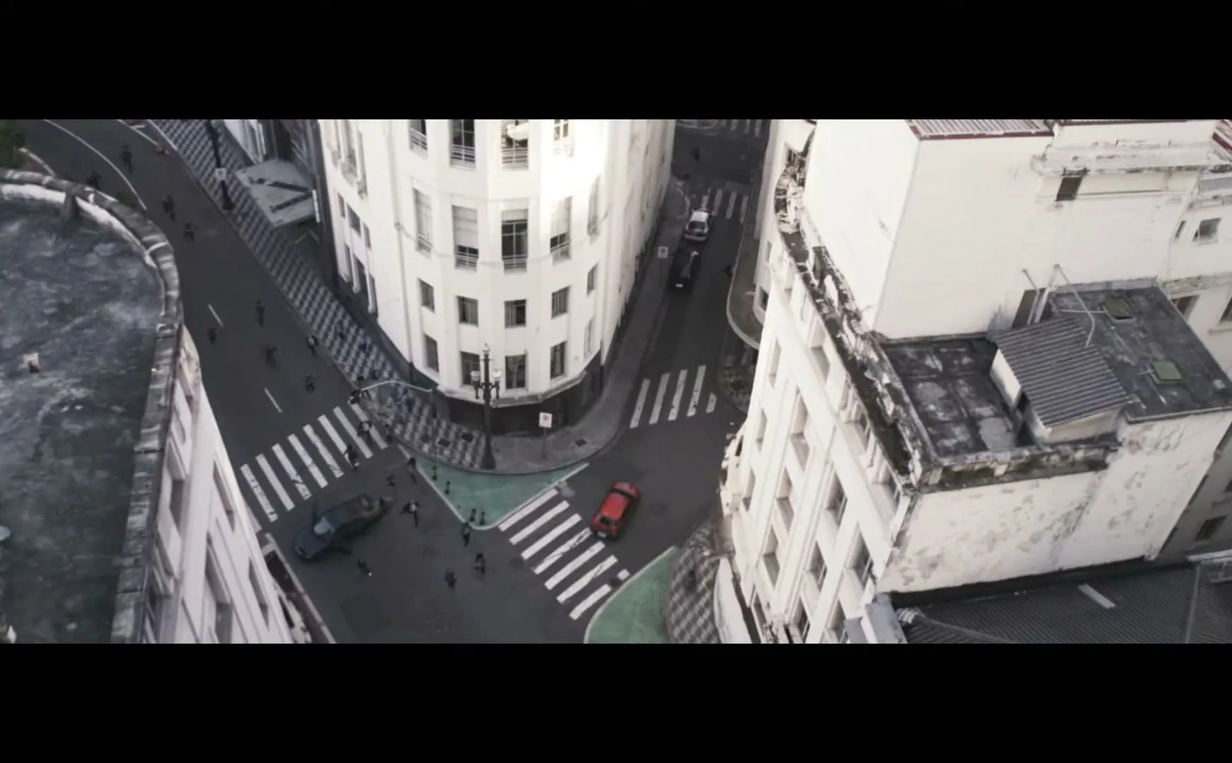 An aerial view shows a red car driving through a busy city intersection with pedestrians and other vehicles.