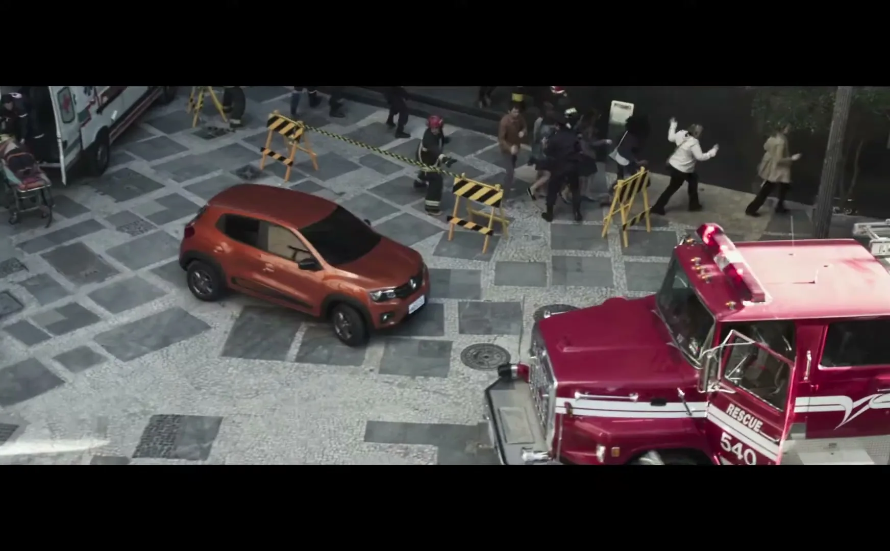 An orange car is parked on a cobblestone street, surrounded by emergency vehicles and people in a chaotic scene.