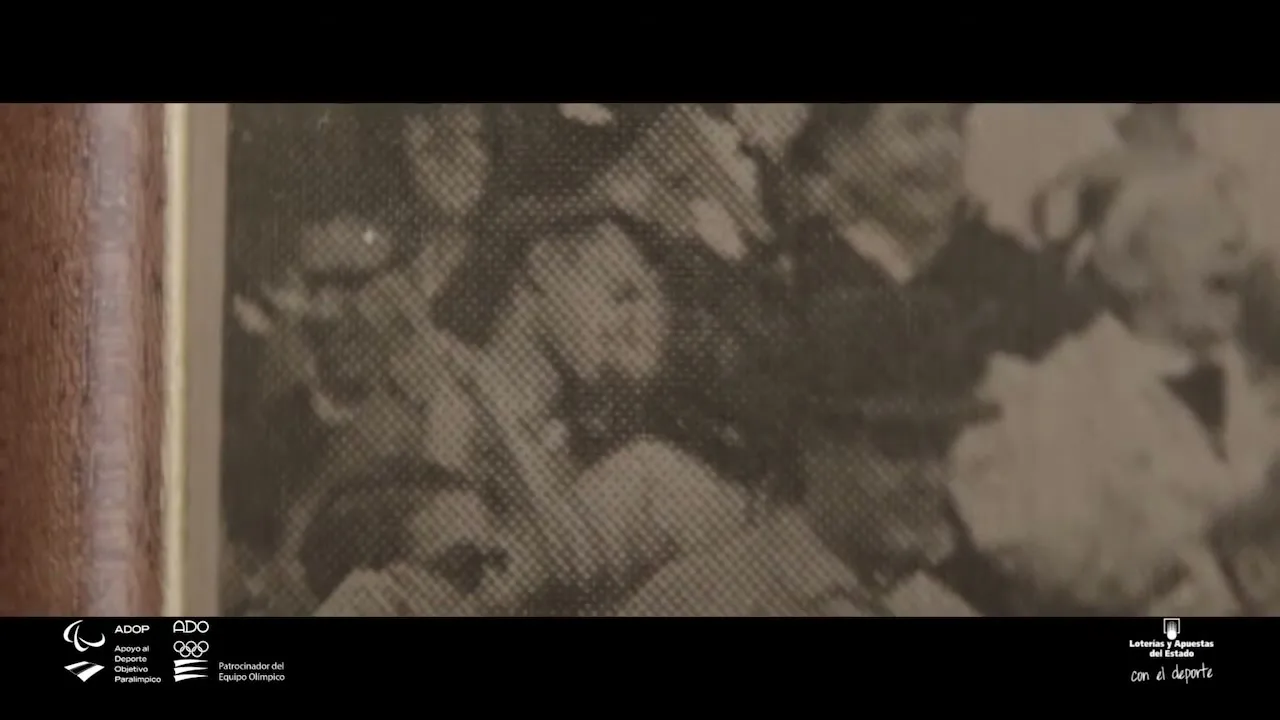 A grainy, black and white archival photo of a crowd of people is shown, with a wooden frame partially visible on the left.