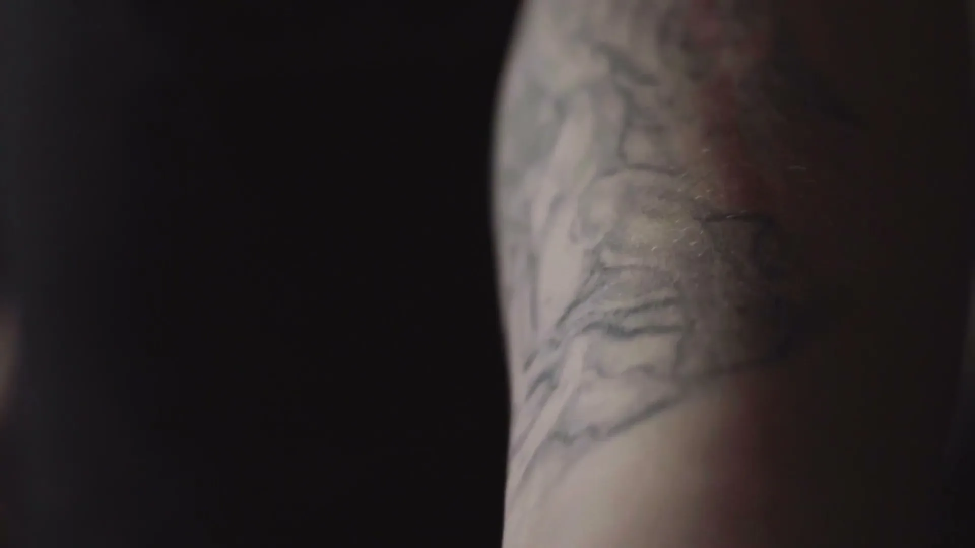 A close-up shot of a person's tattooed arm, with a clenched fist, as the camera slowly pans up the arm.