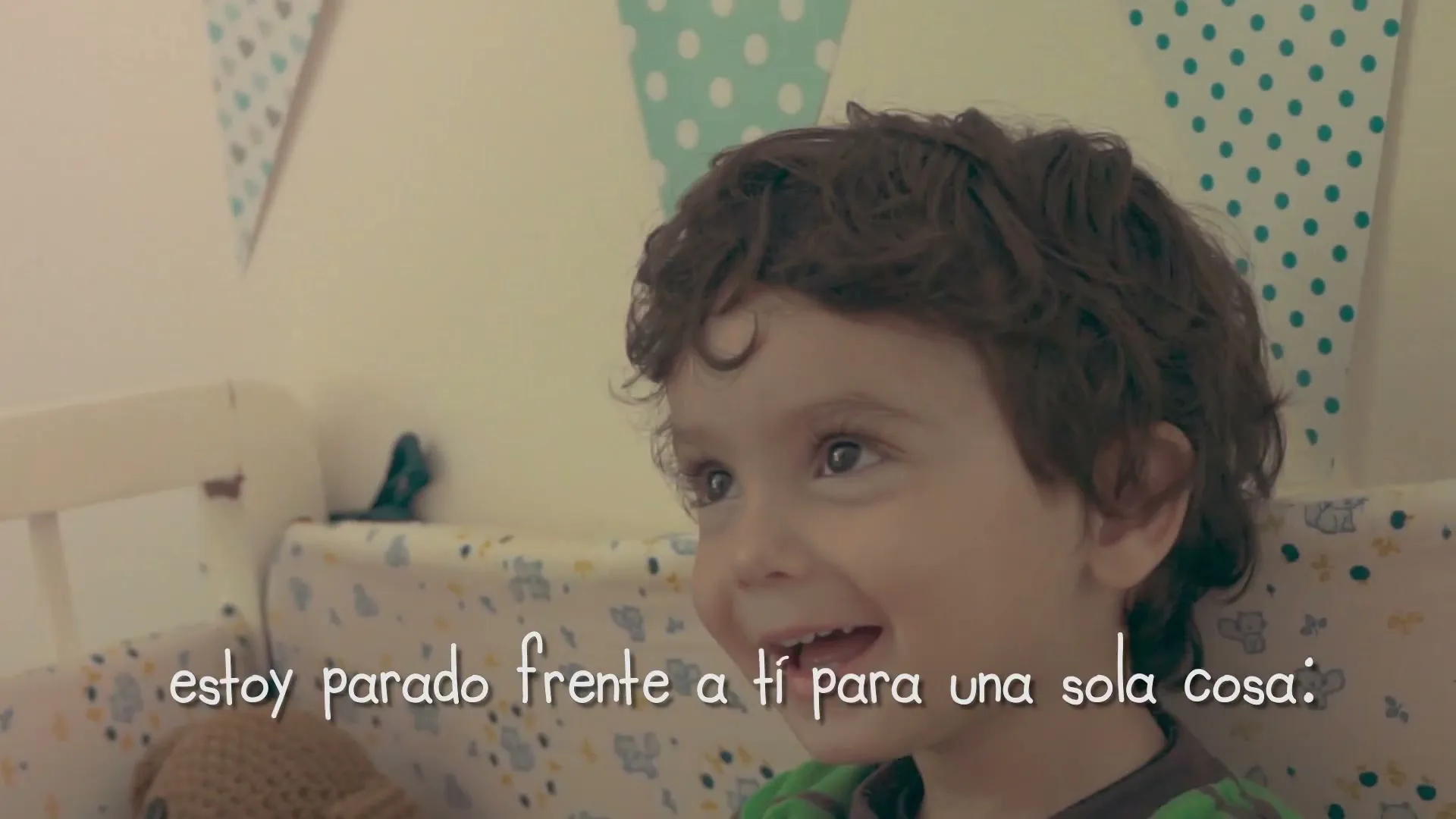 A young boy with curly brown hair smiles happily while standing in a crib, looking up and to the right, with text overlay.