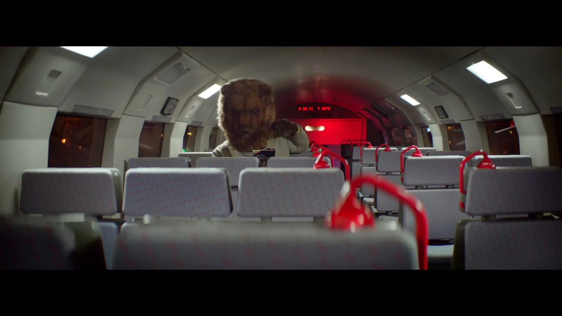 A person in a bear costume sits alone in a train car, looking down at something in their hands.