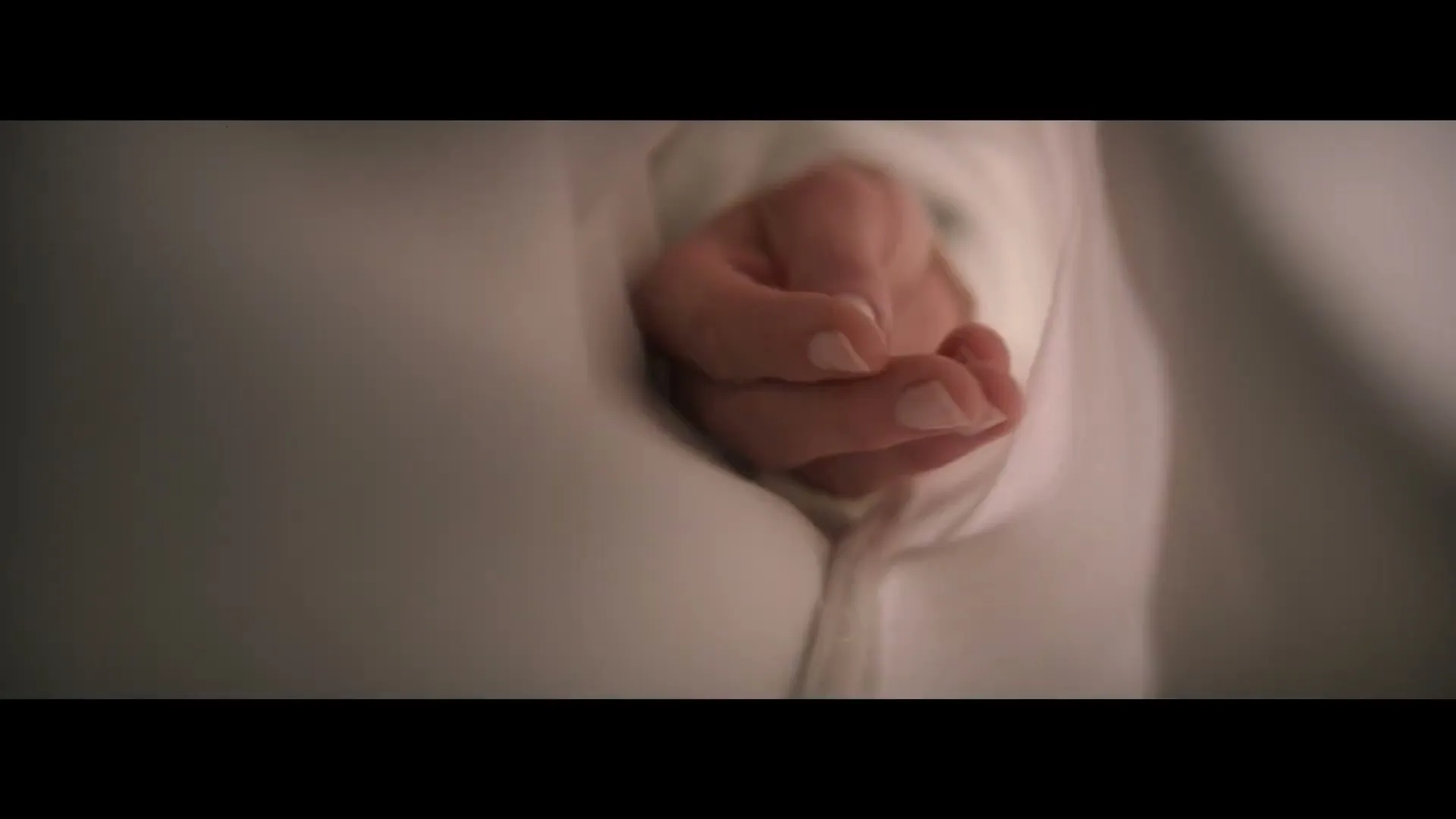 A person's hand, covered by a white sheet, slowly unfurls from a fist to an open palm, suggesting waking up in bed.