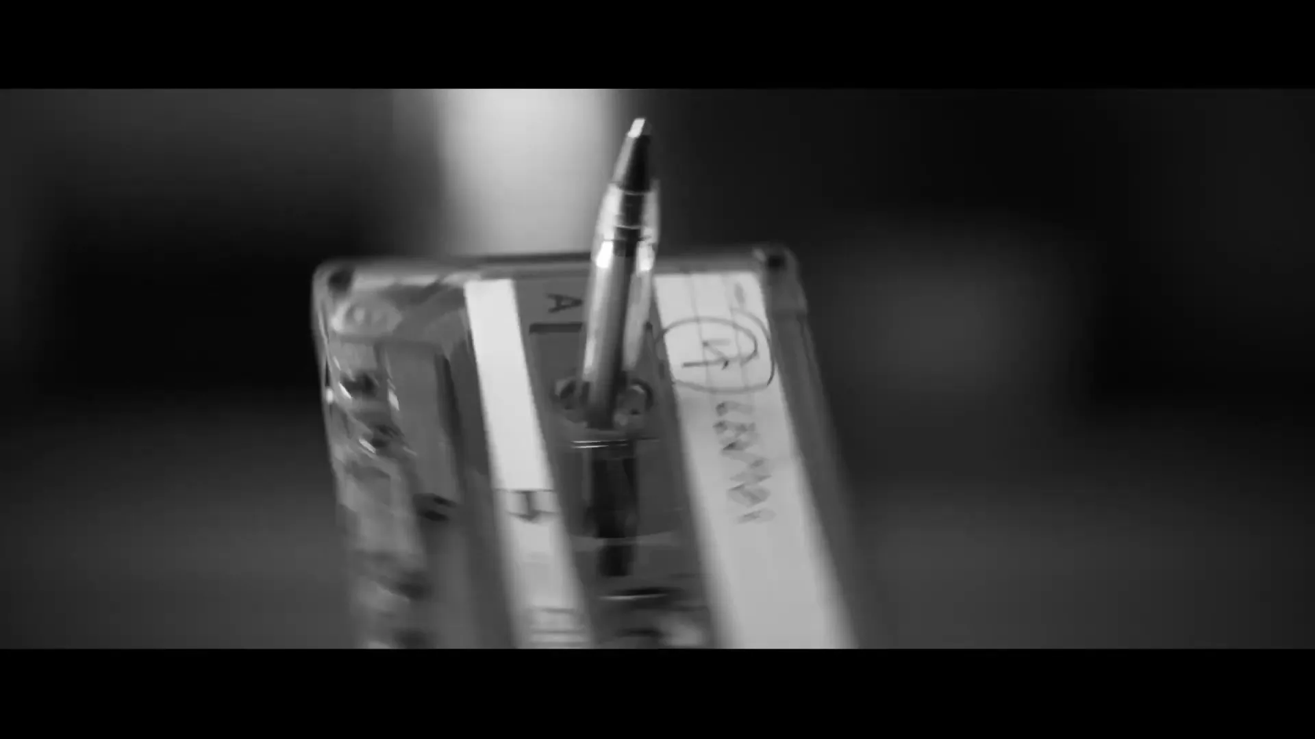 A close-up shot in black and white shows a pen rewinding a cassette tape, a nostalgic act from the past.