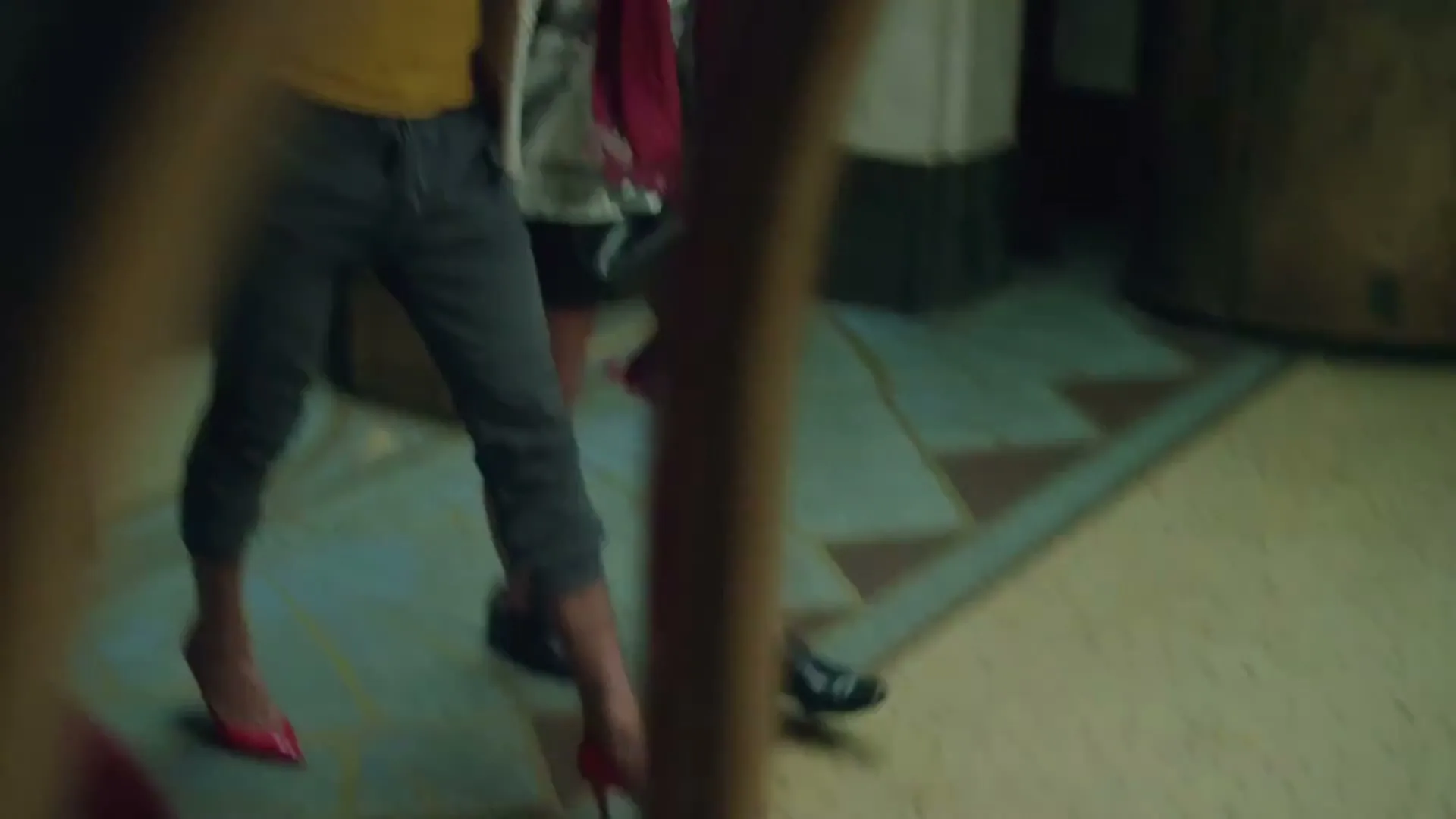 A man in a hat and a woman in a white shirt emerge from an ornate elevator, then walk away, revealing their feet on a tiled floor.