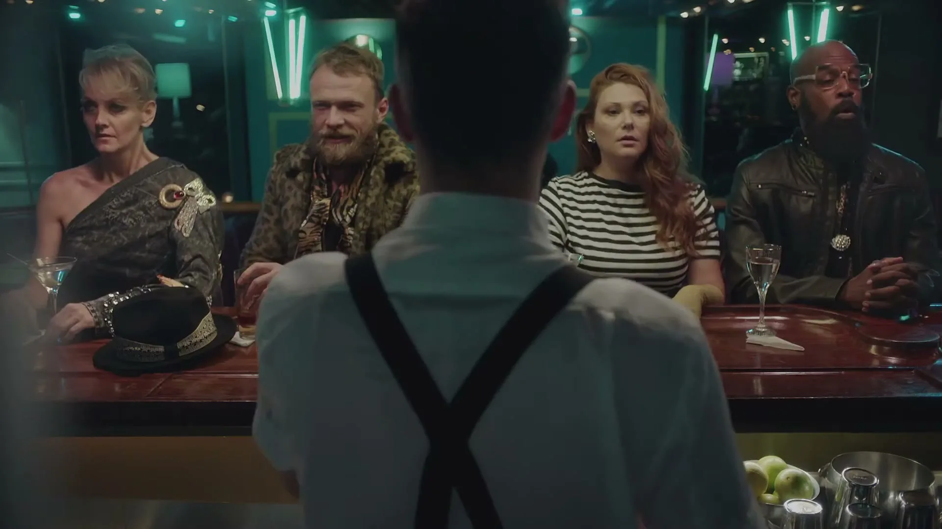 Four diverse people sit at a bar, looking at the bartender from behind, in a dimly lit club.
