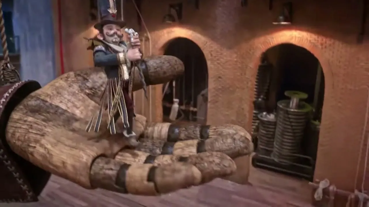 A small, animated man in a top hat and striped coat stands on a giant wooden hand, which lowers him to the ground in a large, brick-walled factory.
