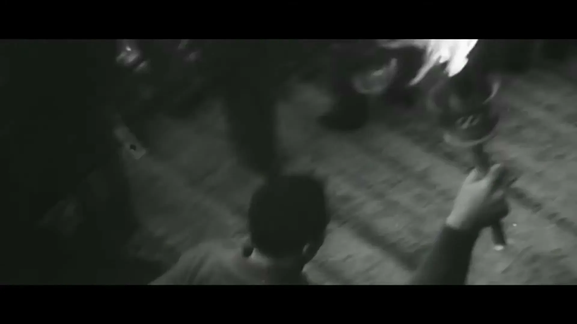 A black and white archival shot shows a person from behind, holding a flaming torch, walking up stairs with other people in the background.