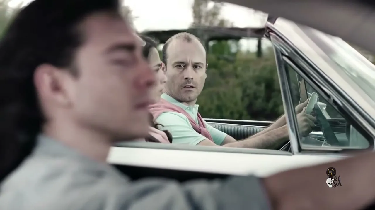 A man with long hair drives a white convertible, while a bald man and a woman in the passenger seat look at him with surprise and envy.