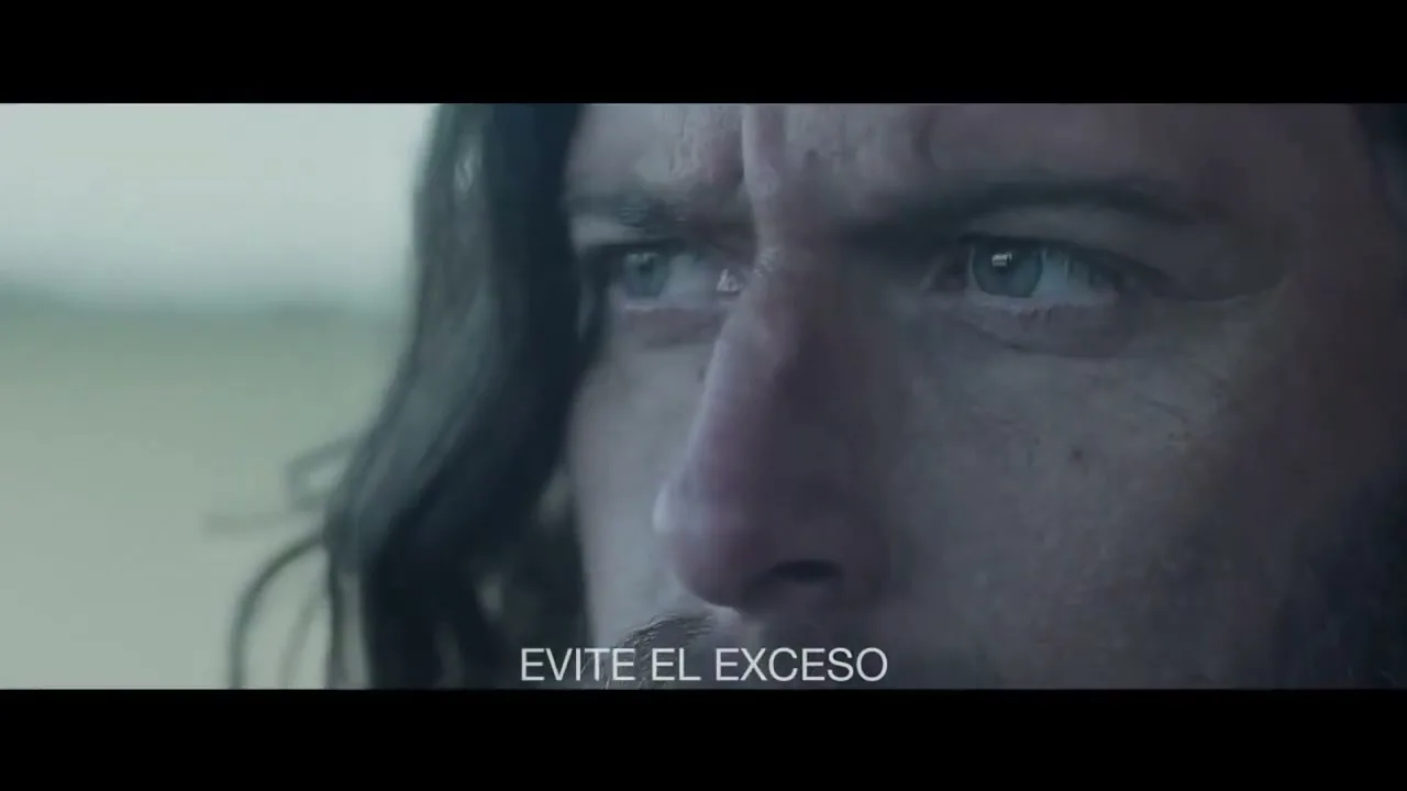 A man with long dark hair and a beard looks intently off-screen, his blue eyes wide with concern, in a close-up shot.