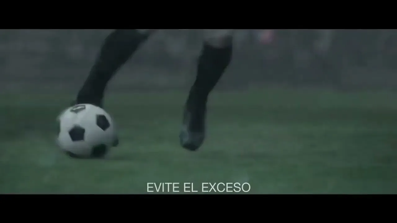 A soccer player's legs are seen kicking a soccer ball on a green field, with other players and stadium lights in the background.