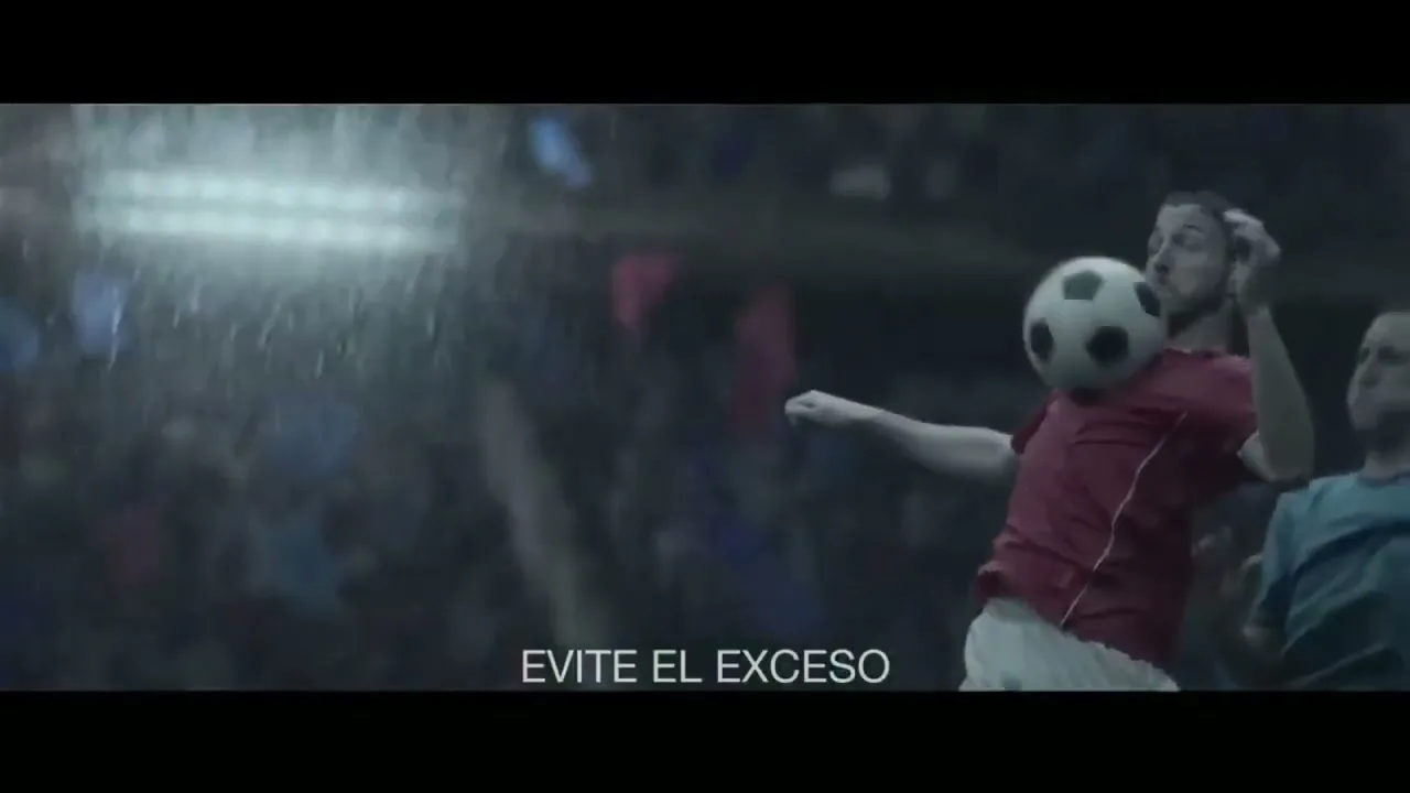 A male soccer player in a red jersey heads a soccer ball during a game in a stadium at night.