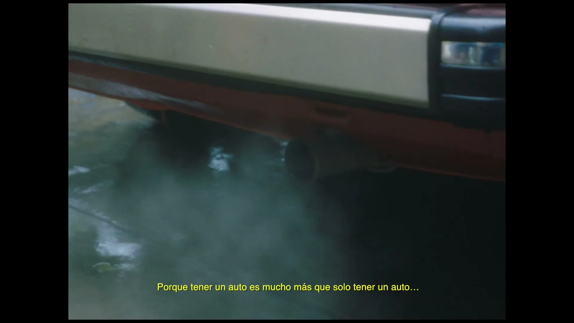 The exhaust pipe of a red car emits smoke, with yellow Spanish subtitles at the bottom of the frame, in an exterior setting.