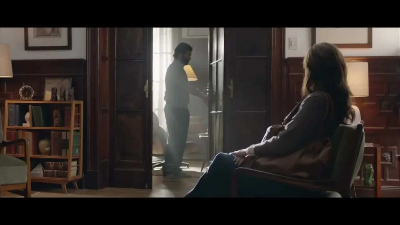 A woman sits in a chair in a dimly lit room, as two men enter through a doorway, one holding a briefcase.