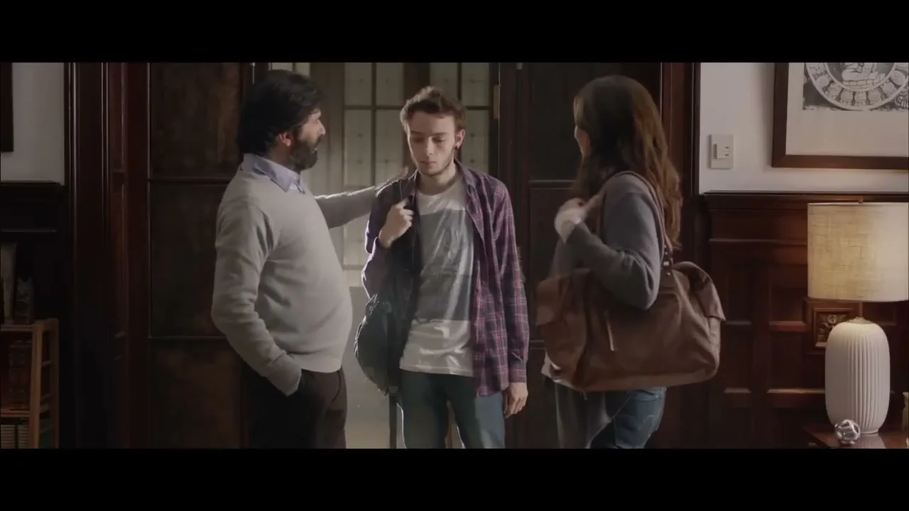 A male psychologist with a beard talks to a teen boy and his mother in a dimly lit office, with the mother holding a large brown bag.