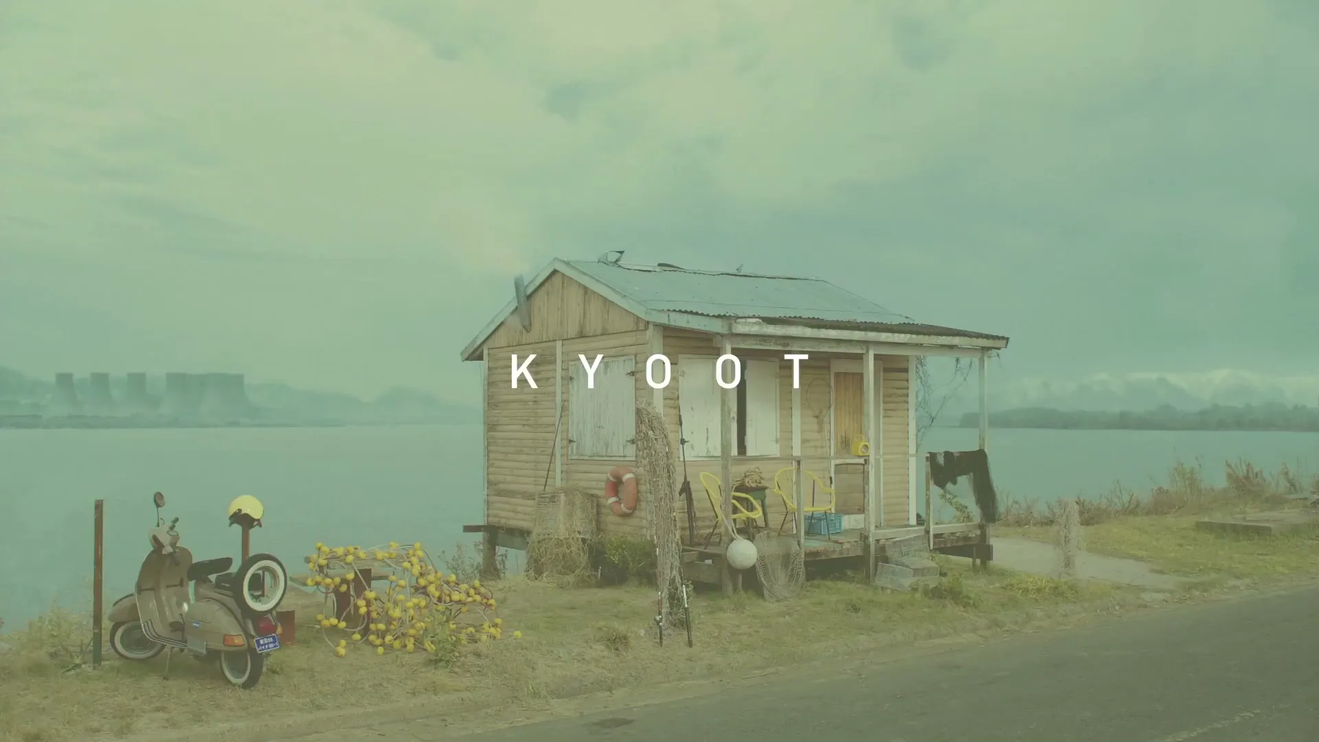 A man in a red shirt waves from a small wooden shack by a lake, with a scooter and lemons outside, under a cloudy sky.