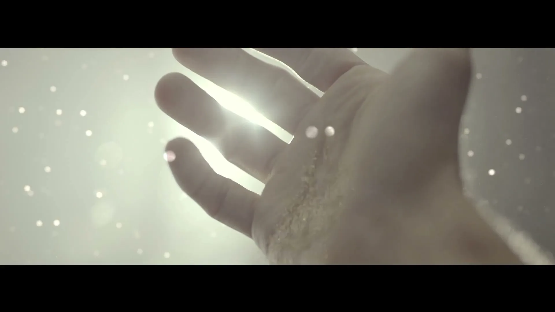 A person's hand is shown reaching up towards a bright light, with small particles floating around, creating a serene and ethereal atmosphere.