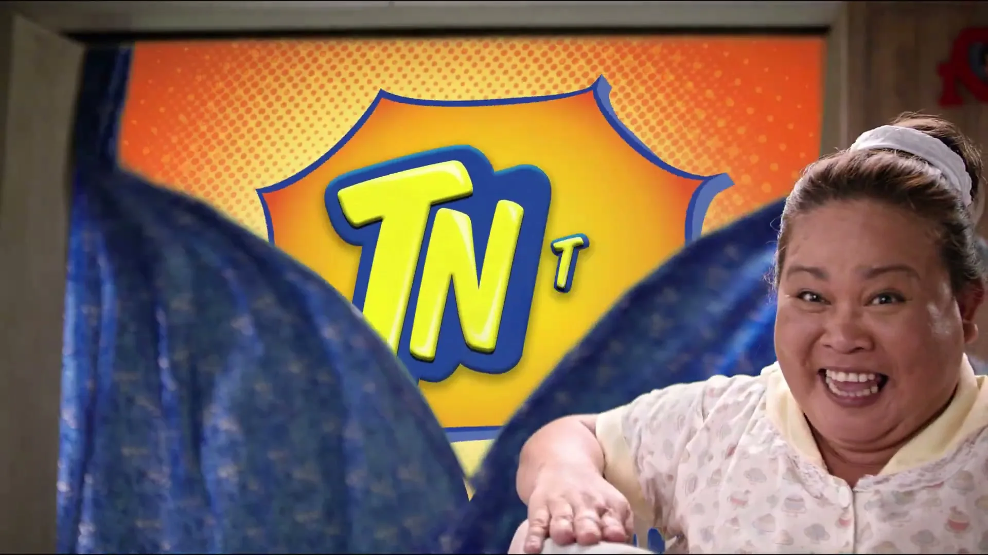 A woman in her 40s, wearing a house dress, pulls back a blue curtain to reveal the TNT logo in a comic book style.