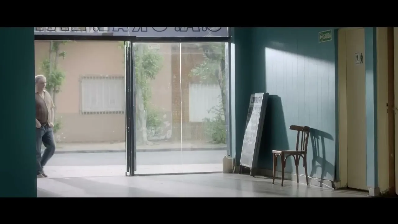 A middle-aged man with a beard and casual clothes walks into an empty room from outside, looking around with a neutral expression.