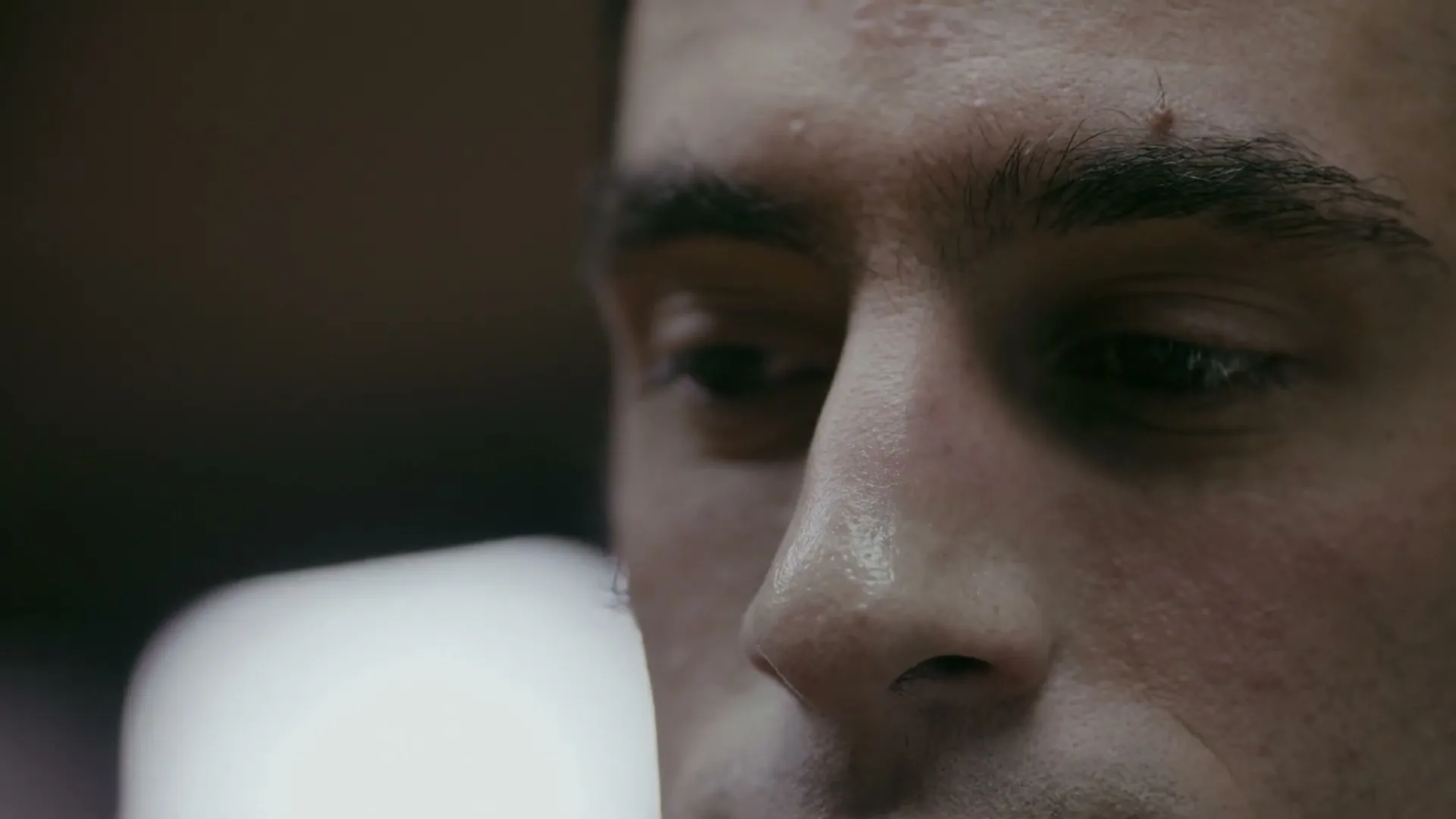 A sweaty male athlete with dark hair looks down, deep in thought, in a dimly lit interior setting.