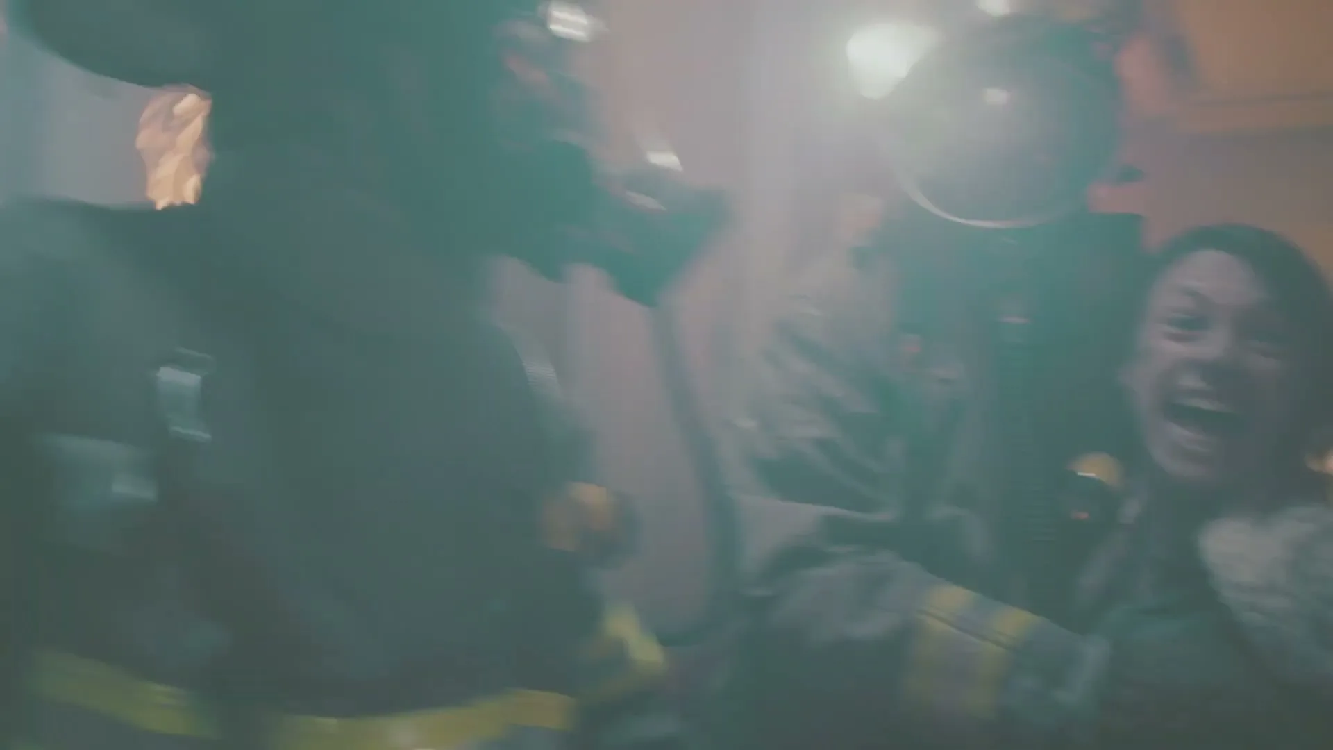 A woman in a beige sweater is rescued from a burning building by two firefighters, who lead her through a smoky doorway.