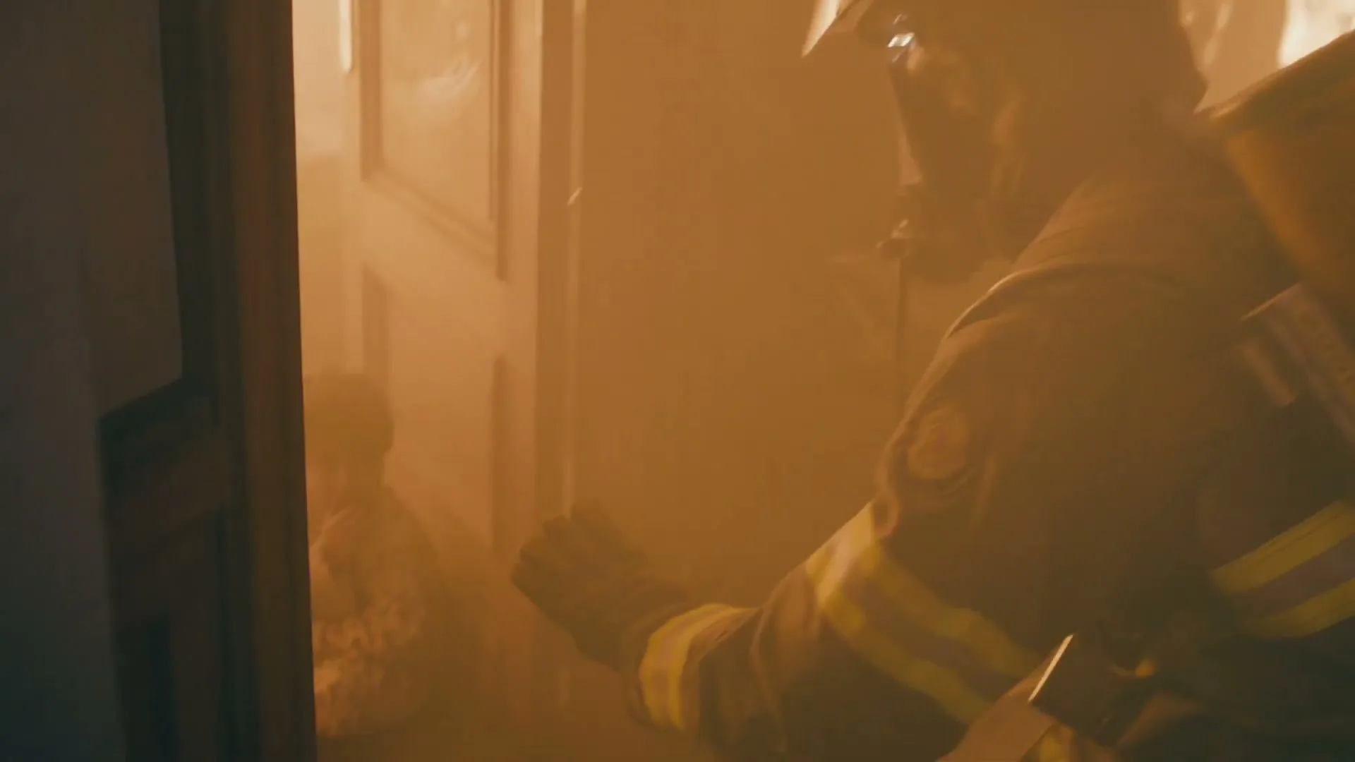 A firefighter in full gear enters a smoke-filled room and finds a small child sitting on the floor, reaching out to them.