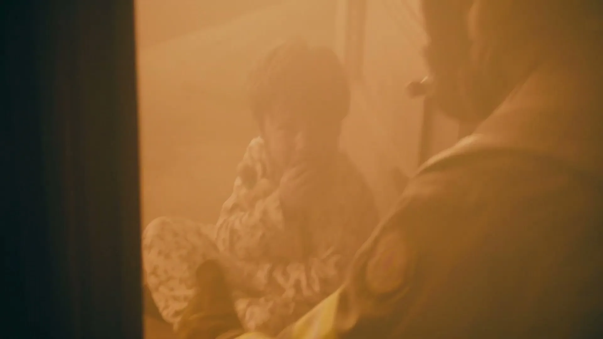 A firefighter in a smoky room holds a small child in patterned pajamas, who looks scared and clutches their hands to their face.