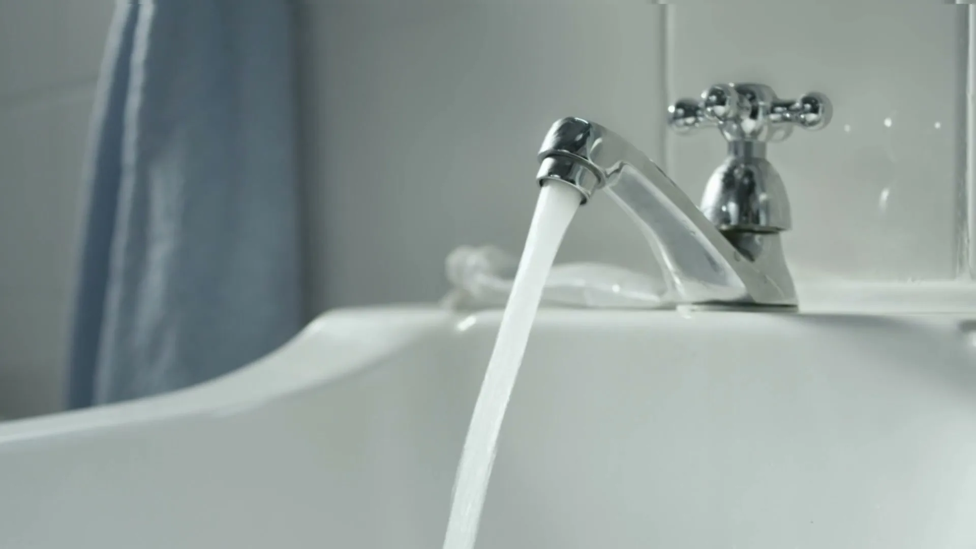 A person's hand reaches for a glass under a running faucet in a clean, white bathroom sink.