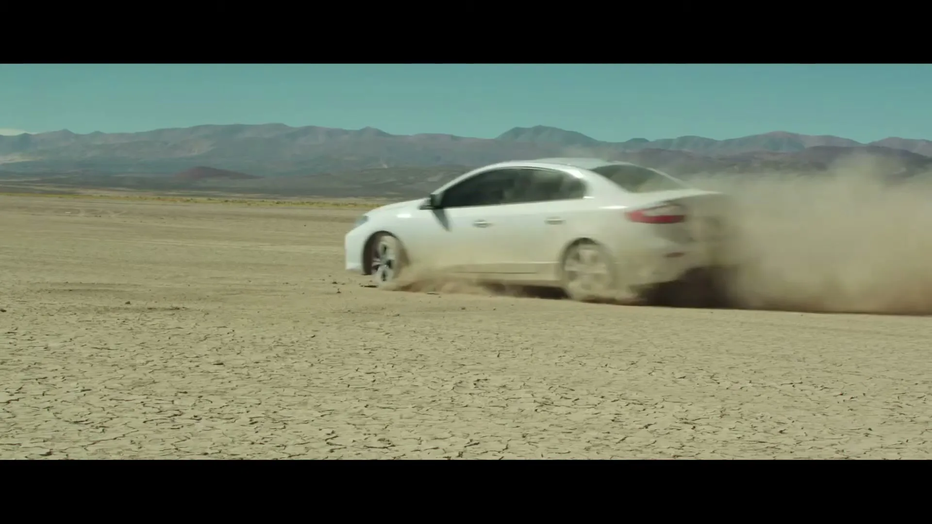 A white car drifts on a cracked desert floor, kicking up dust, with mountains in the background under a clear sky.