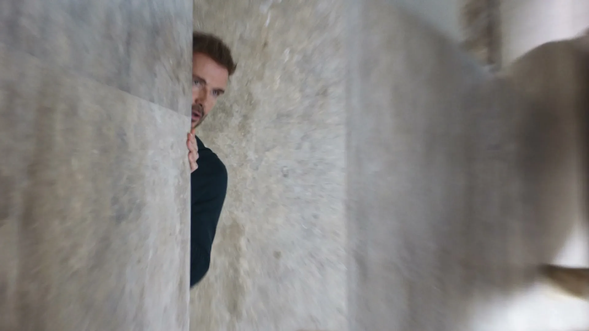 David Beckham peeks around a corner, looking surprised and slightly confused, in a modern, luxurious interior.