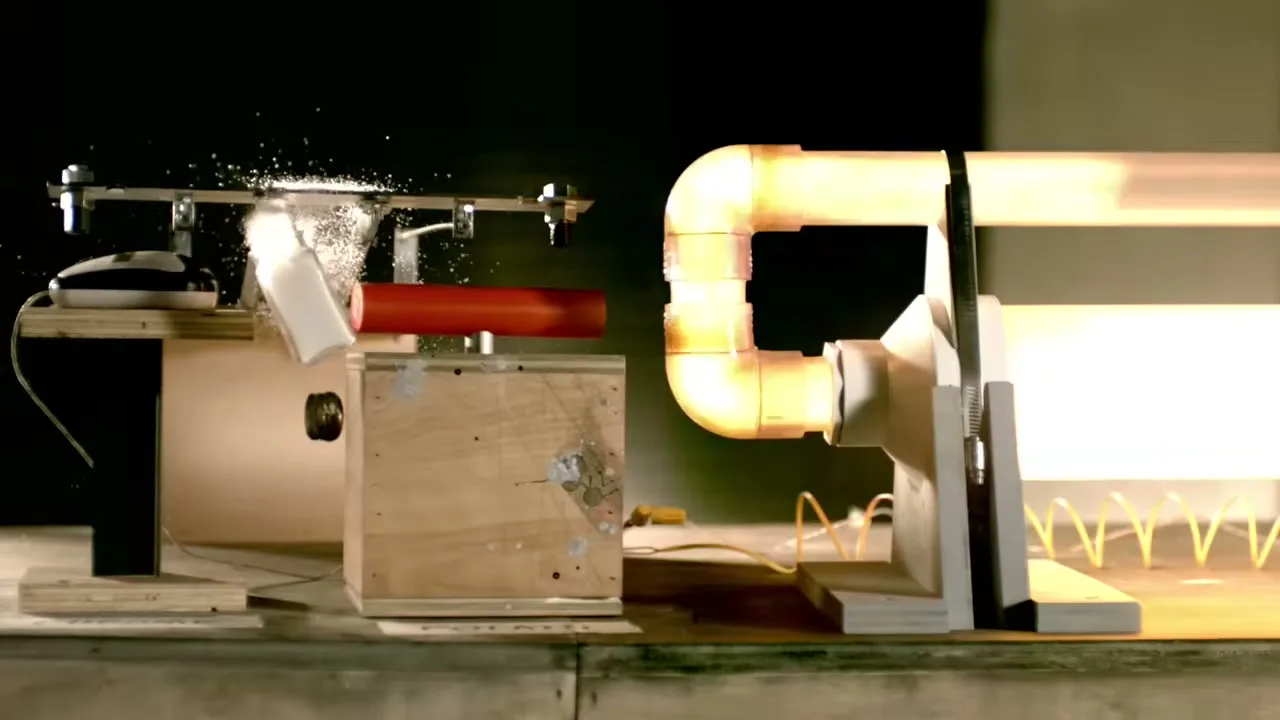 A white object is launched from a red tube, shattering into many pieces as it hits a metal bar, with a bright light tube on the right.