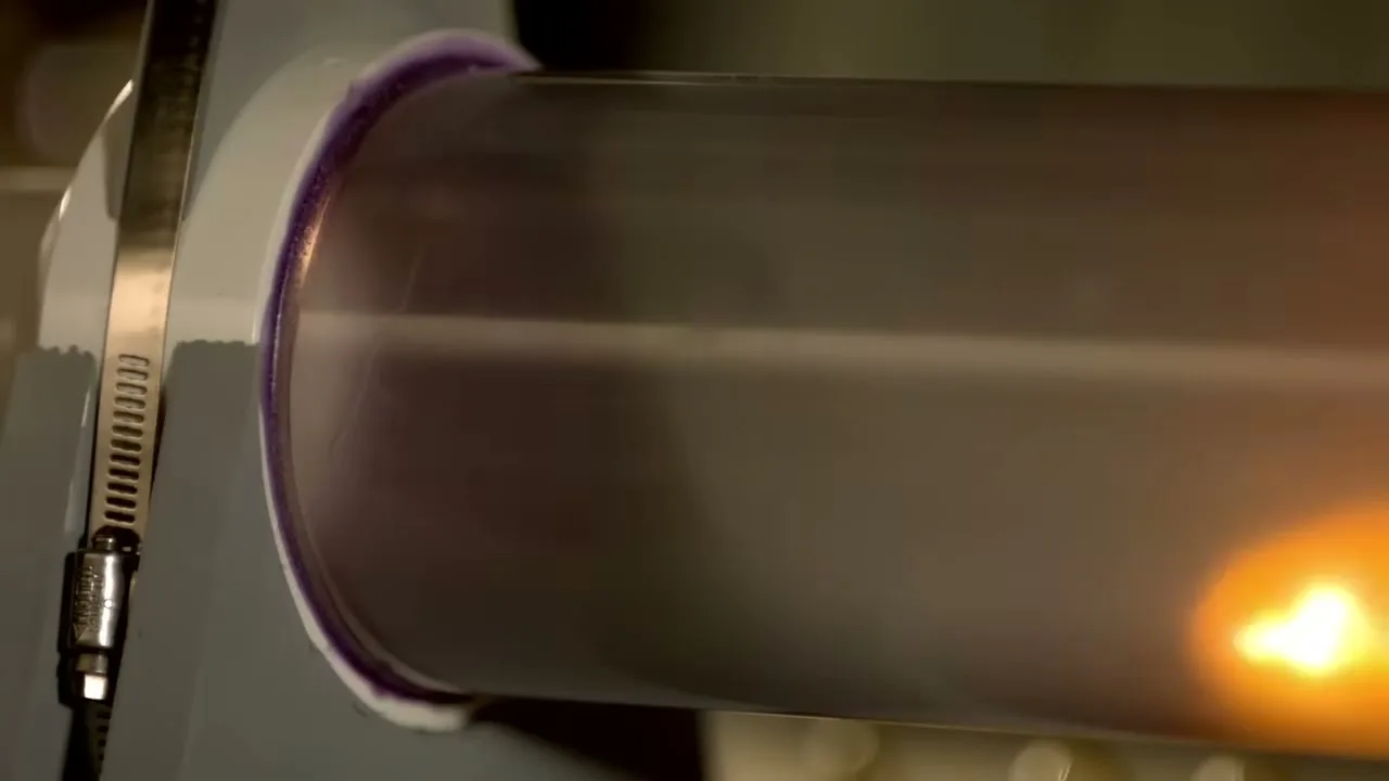 A close-up shot shows a clear tube with a purple ring, as a bright orange liquid flows through it.