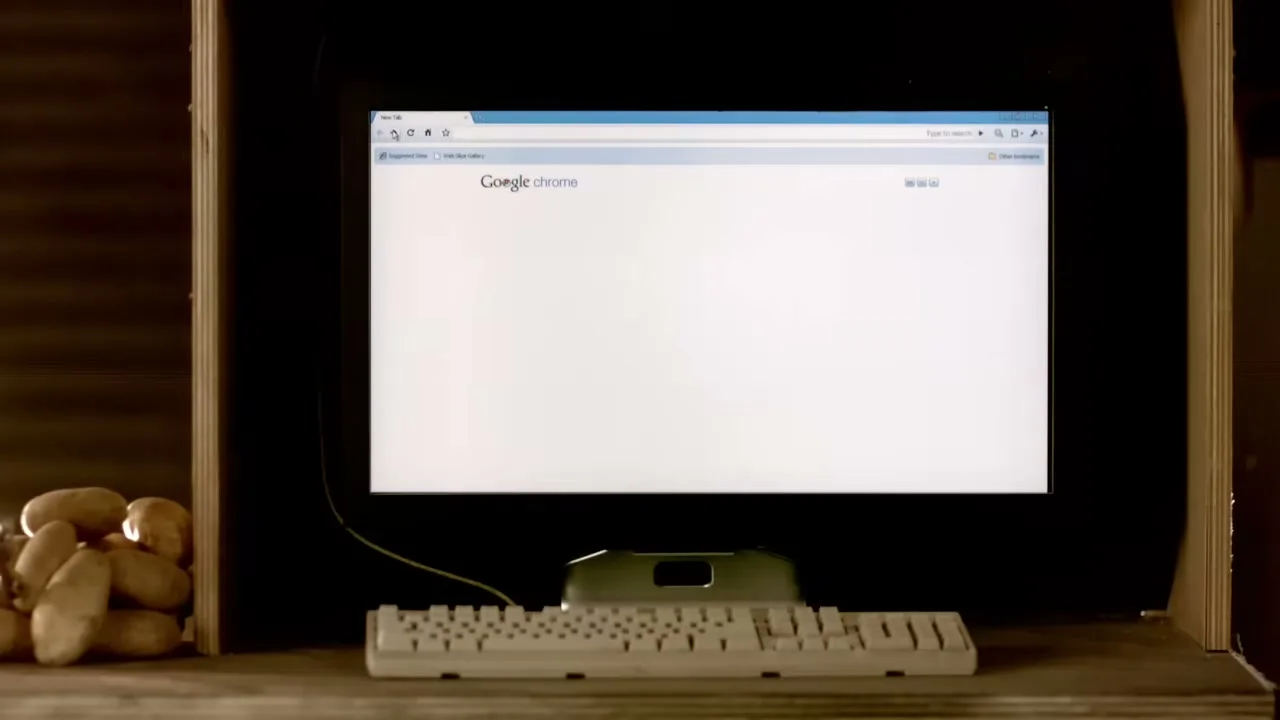 A computer monitor displays the Google Chrome browser with a blank page, while potatoes sit on a shelf next to it.