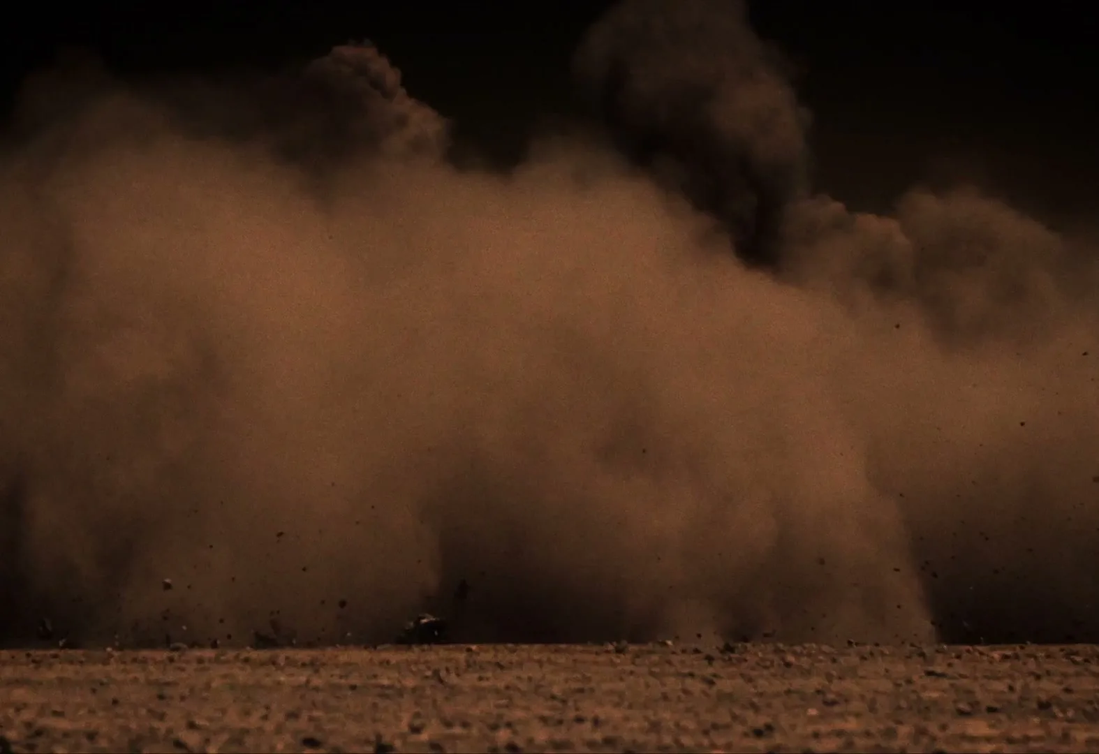 A low-angle shot captures a massive cloud of reddish-brown dust and debris exploding upwards and outwards from the ground, obscuring the view.