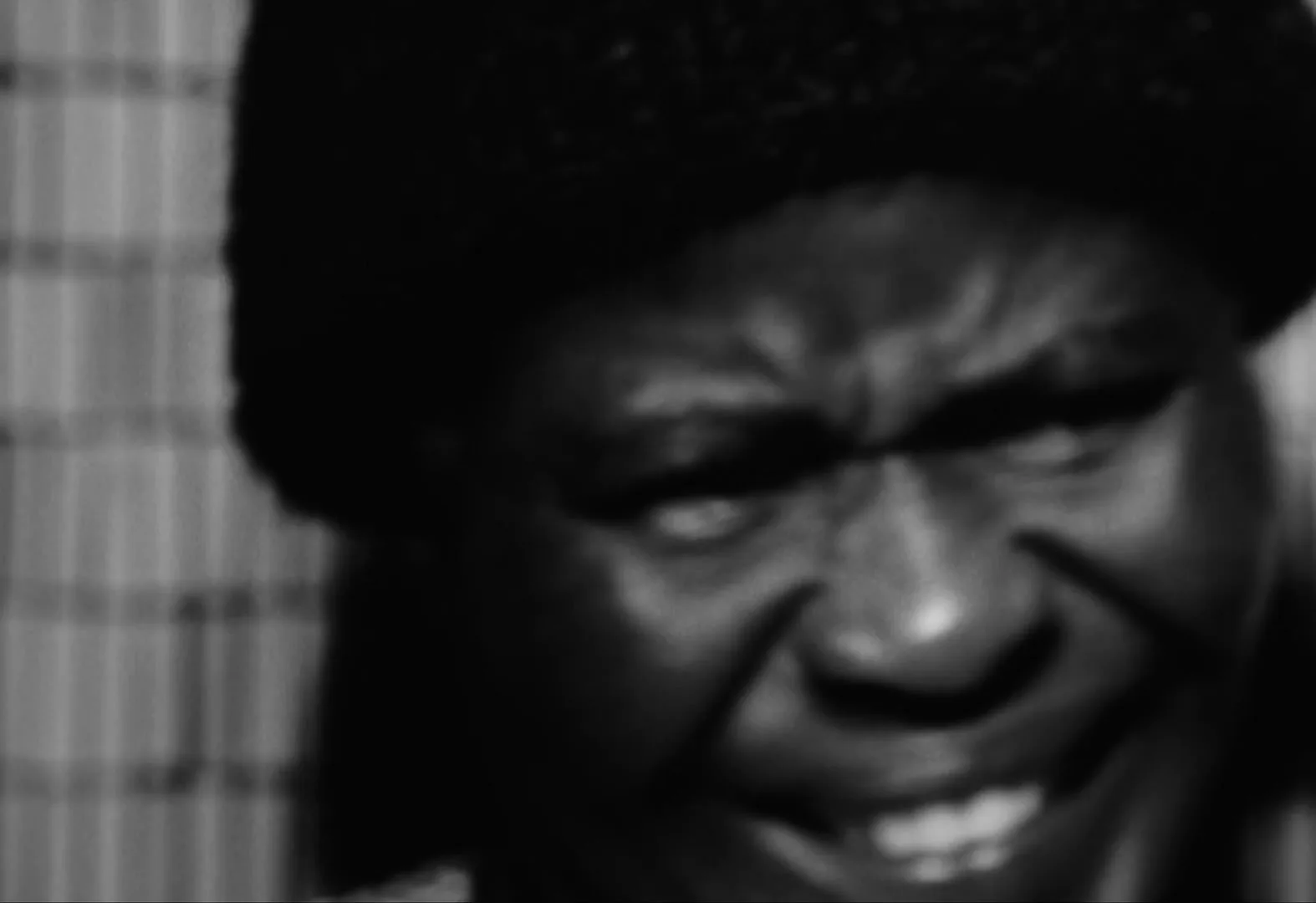 A black and white extreme closeup shows a person with a furrowed brow and a slight smile, looking intensely at something off-camera.