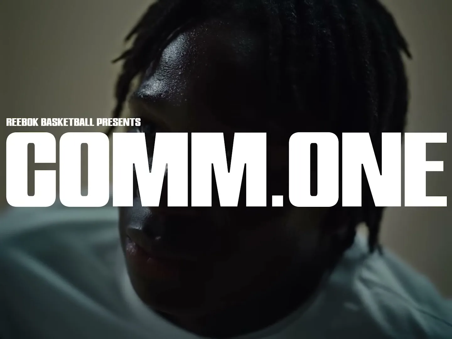 A dark-skinned man with dreadlocks and a white shirt looks down, with "REEBOK BASKETBALL PRESENTS COMM.ONE" text overlaying his face.