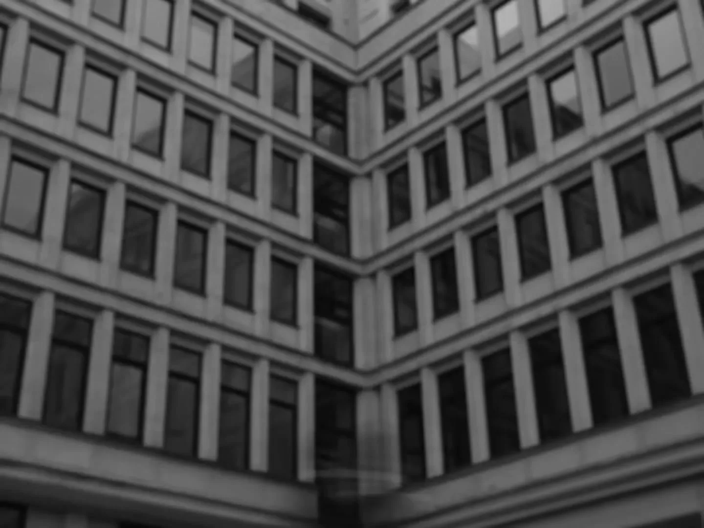 A black and white, blurry shot of a building with many windows, with a dark, blurry shape moving across the frame.