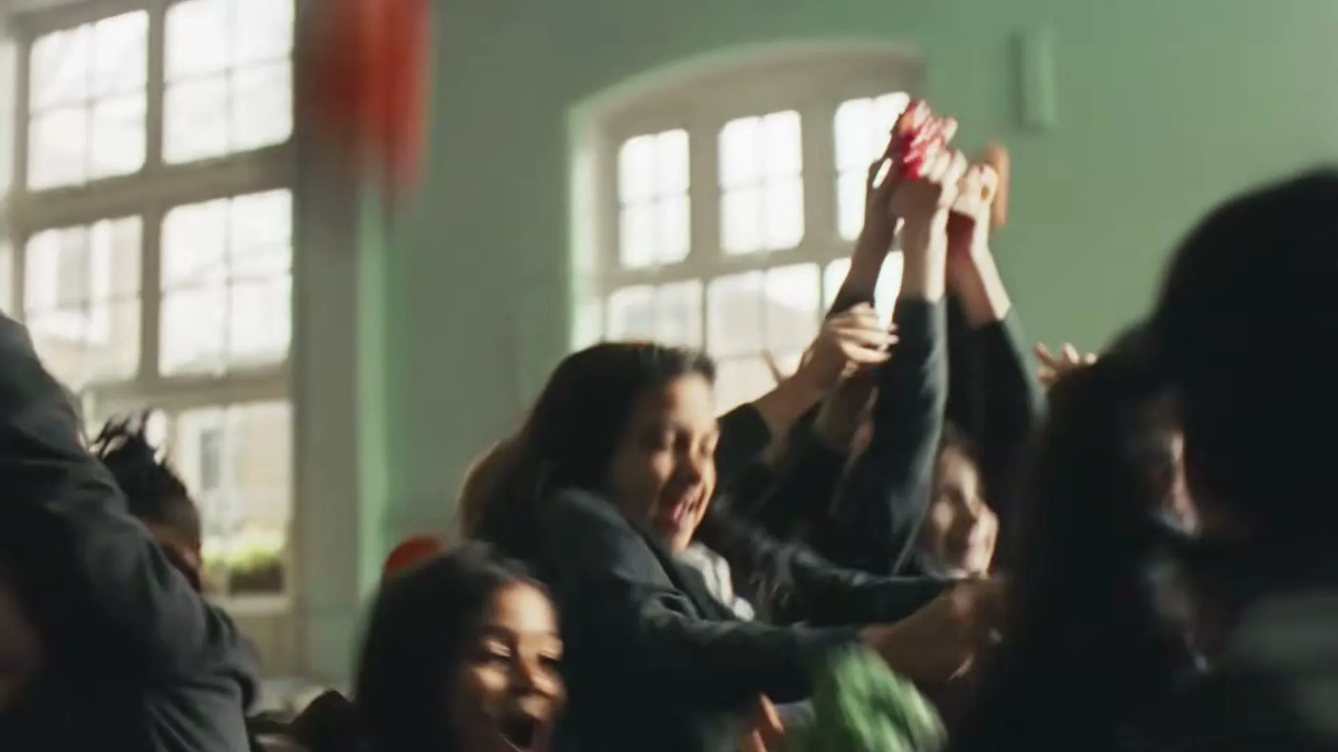 A diverse group of children in school uniforms excitedly reach for fruit and vegetables thrown into the air in a school hall.