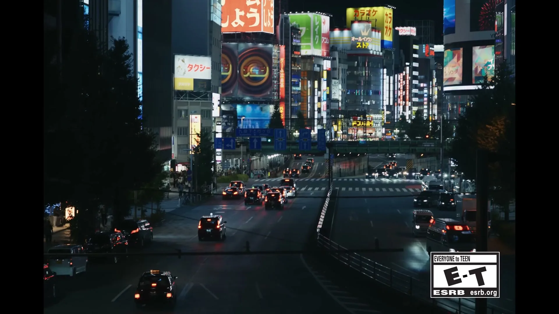 A wide shot of a busy city street at night, with cars driving and bright neon signs illuminating the buildings.