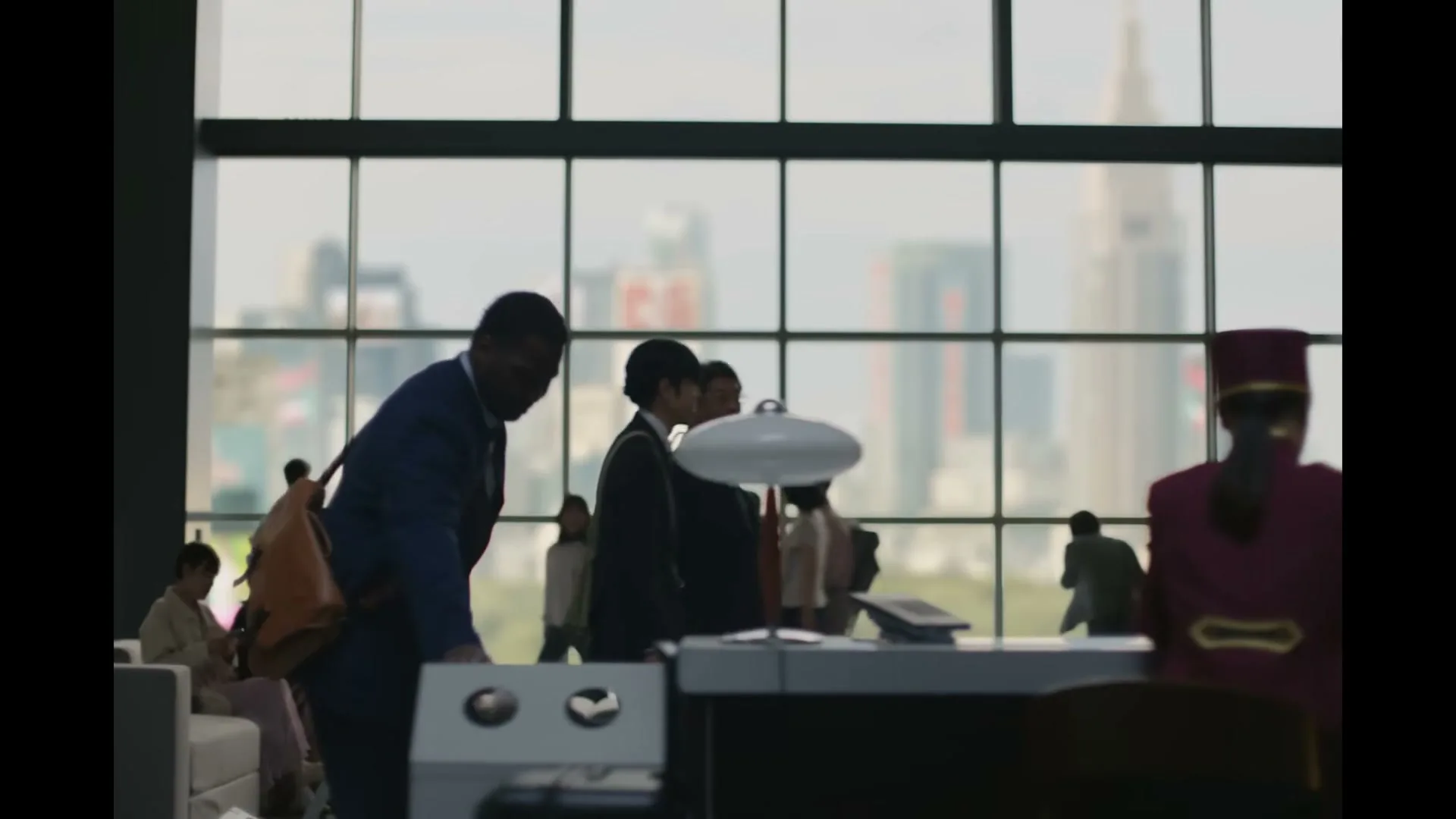 A diverse group of business people walk through a modern office lobby with a city skyline visible through large windows.