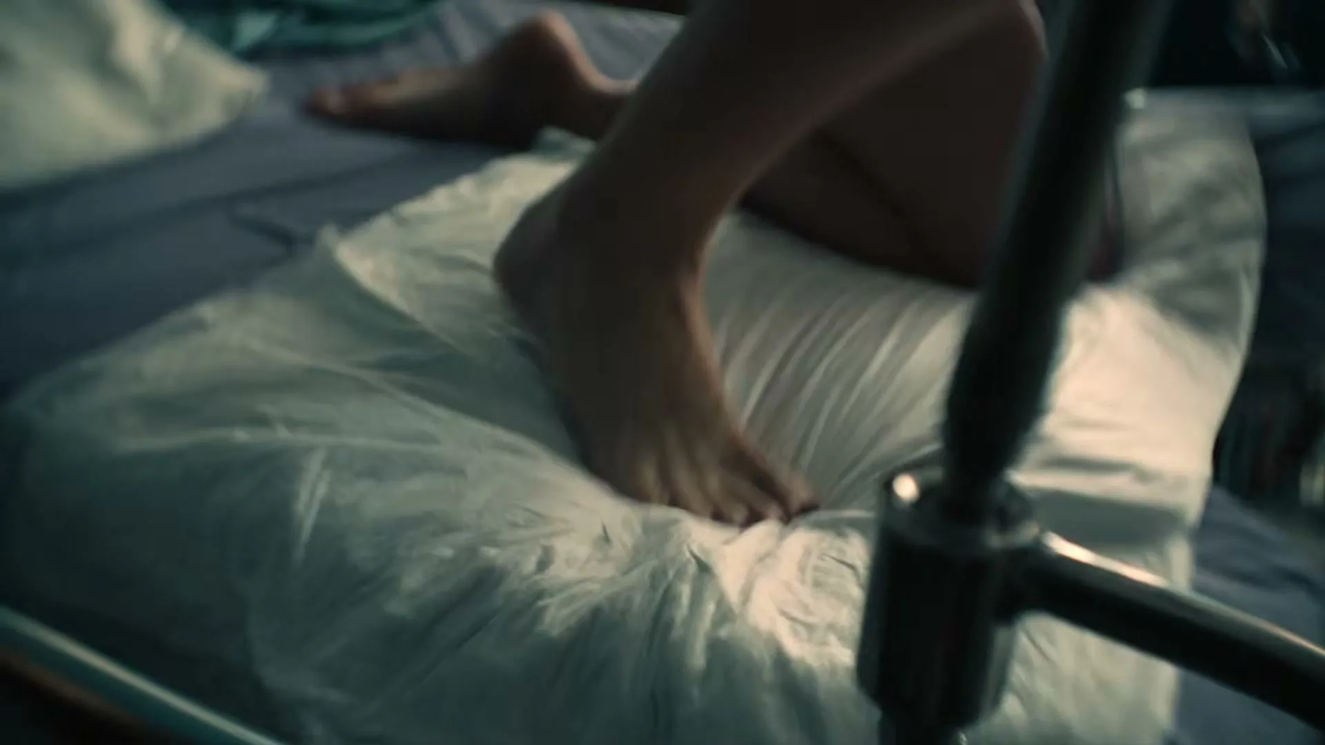 A woman's bare feet push down on a white pillow on a bed, as she appears to be in labor in a hospital room.