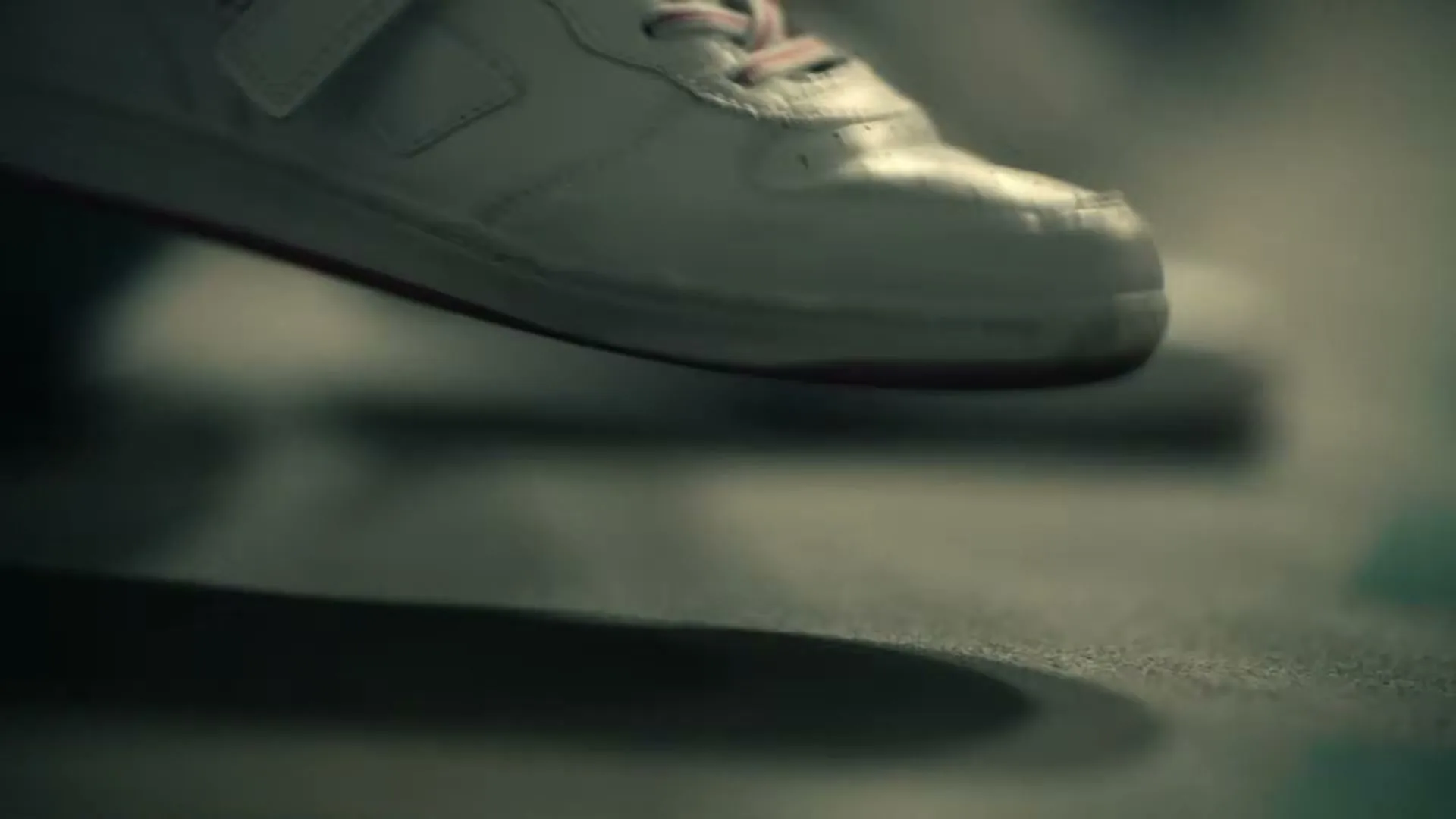A person's feet in white sneakers are seen from a low angle, tapping nervously on a dark floor in an interior setting.