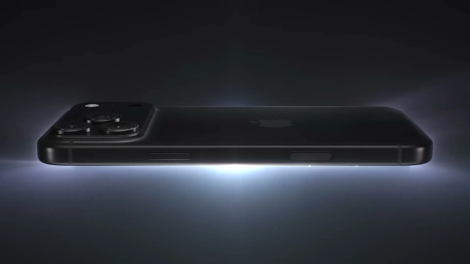 A black iPhone with multiple cameras on its back is shown in a dark studio, with a bright light emanating from beneath it.