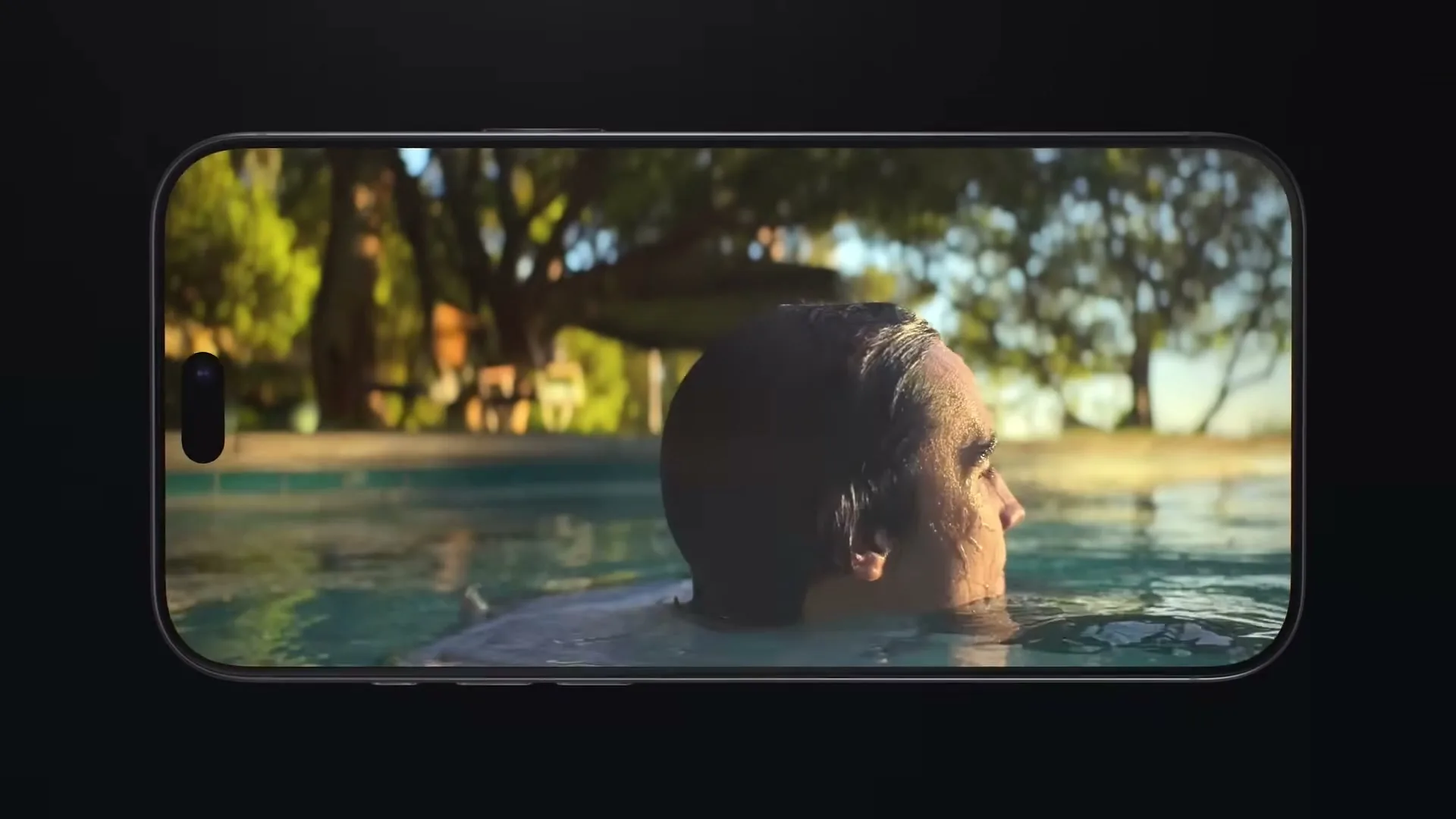 A man with wet hair is seen from the side, looking up, as he floats in a swimming pool, displayed on an iPhone screen.