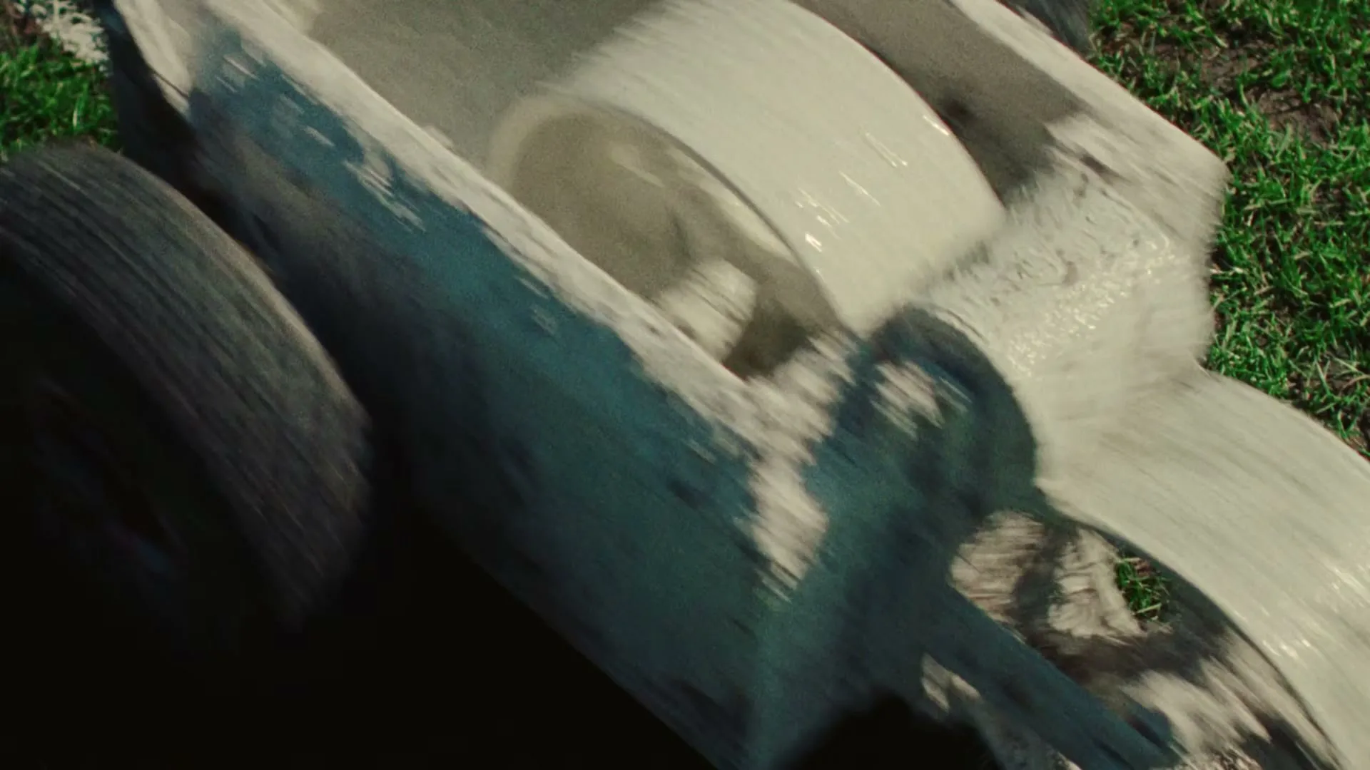A close-up, high-angle shot shows a white line marker being pushed across a green grass field, leaving a trail of white powder.