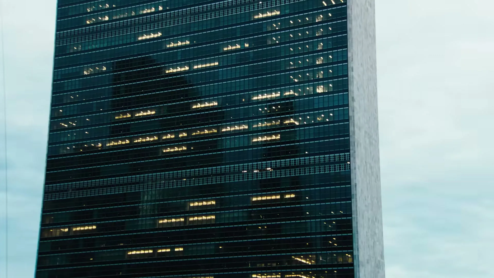 A tall, modern skyscraper with many windows, some lit up, stands against a light blue sky, showcasing urban architecture.
